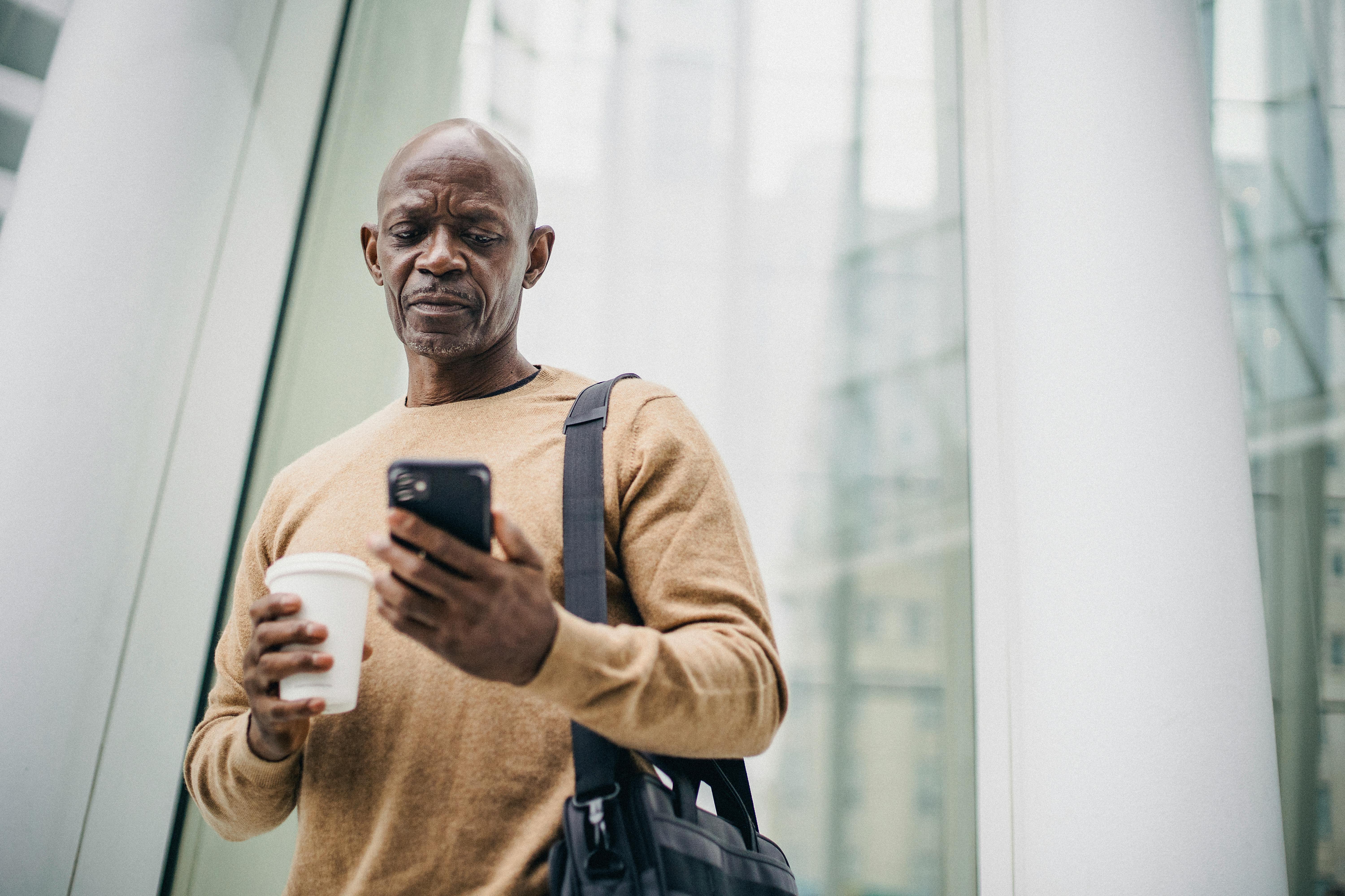 An older man looking sad while looking at his phone while holding a beverage | Source: Pexels