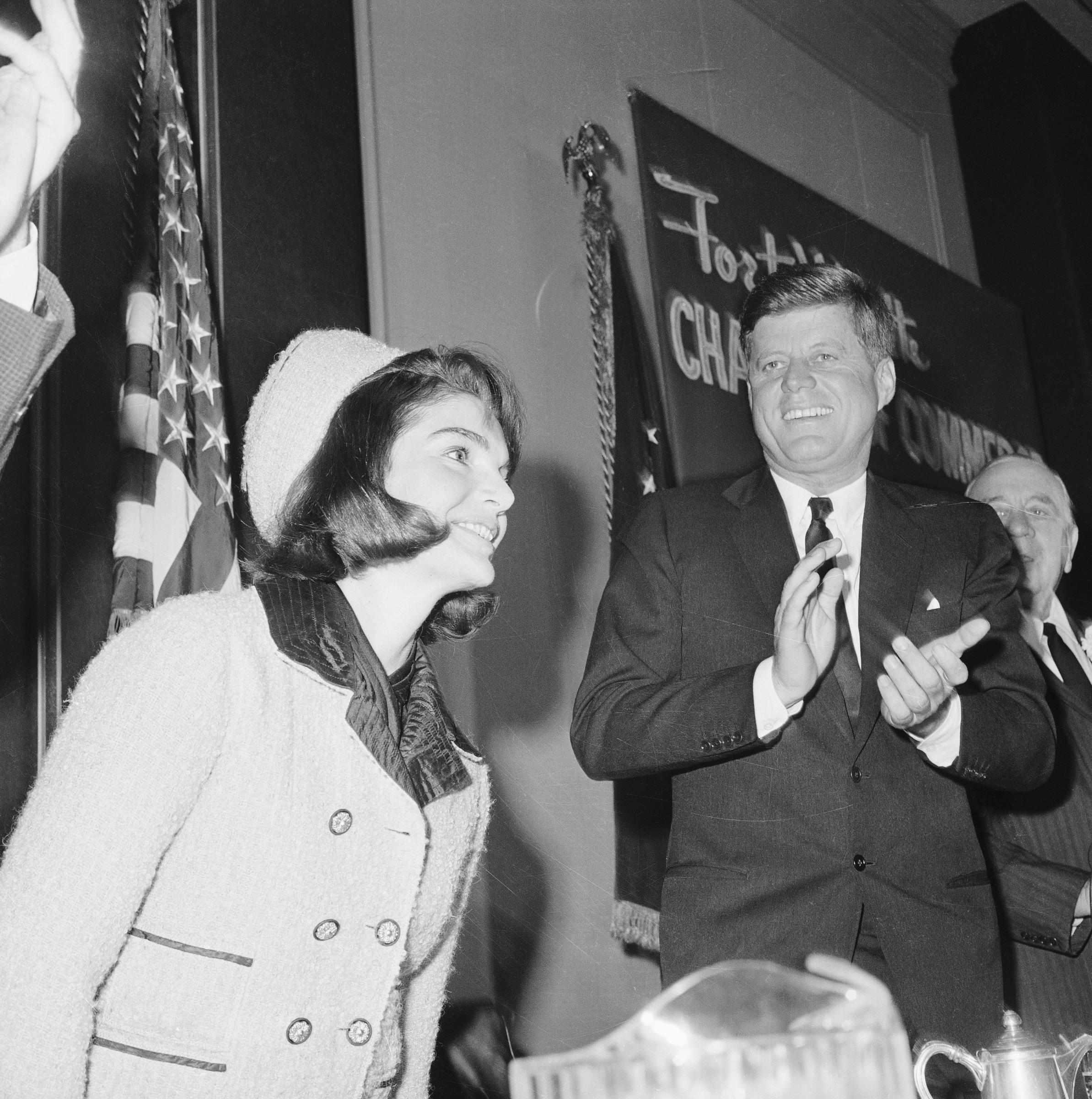 President John F. Kennedy applauds as his wife, First Lady Jackie Kennedy, is introduced at a Chamber of Commerce breakfast on November 22, 1963. | Source: Getty Images