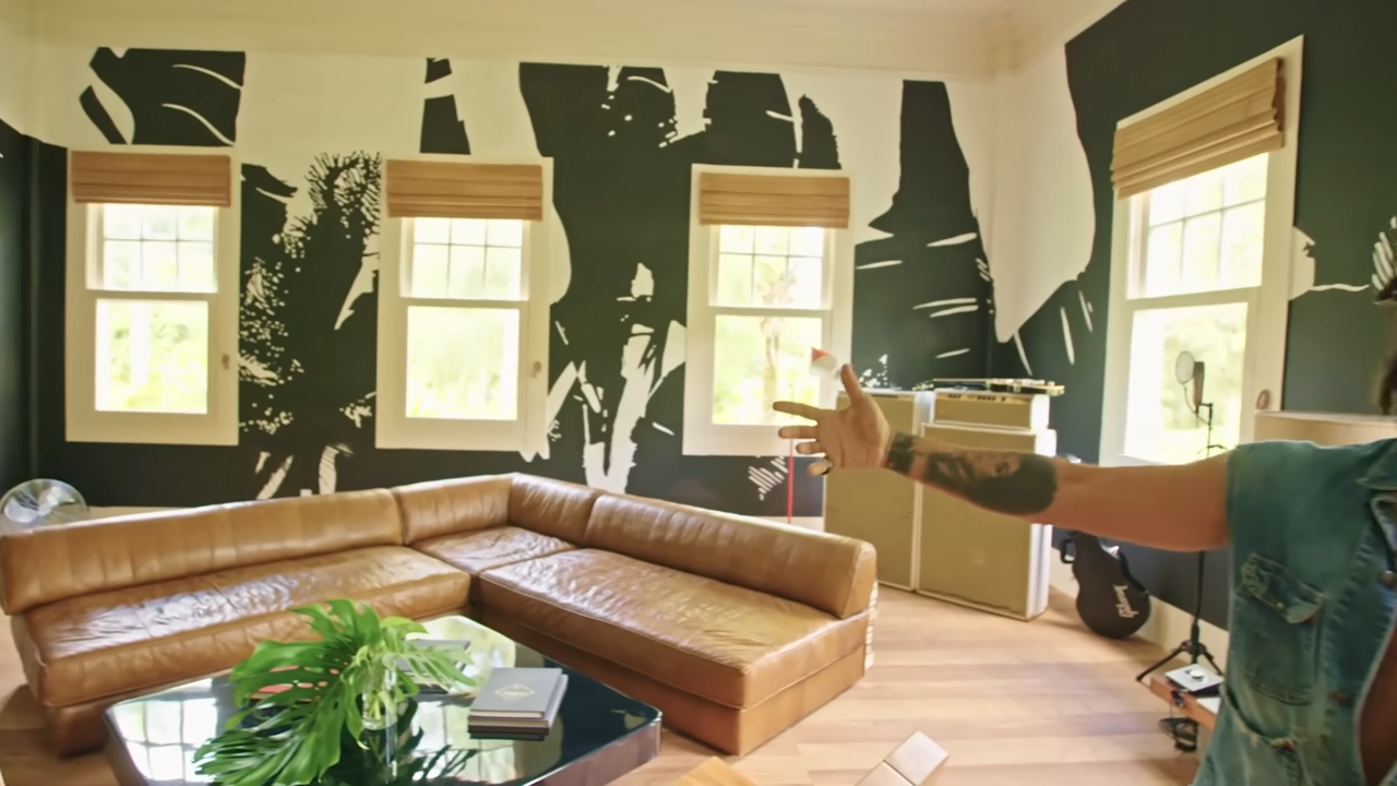 An open-concept view of the bedroom lounge, featuring bold black-and-white botanical wall murals, a low-slung leather sectional, and a glass-top coffee table. | Source: YouTube/@Archdigest