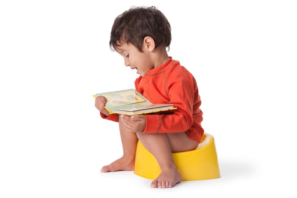 A toddler boy sitting on a potty and reading a book. | Photo: Shutterstock