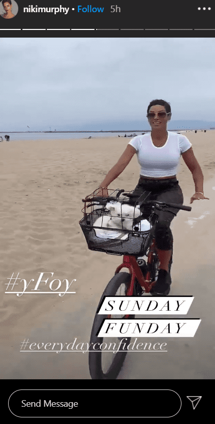 A photo of Nicole Murphy in a white T-shirt cycling with her puppy. | Photo: Instagram/Nikimurphy
