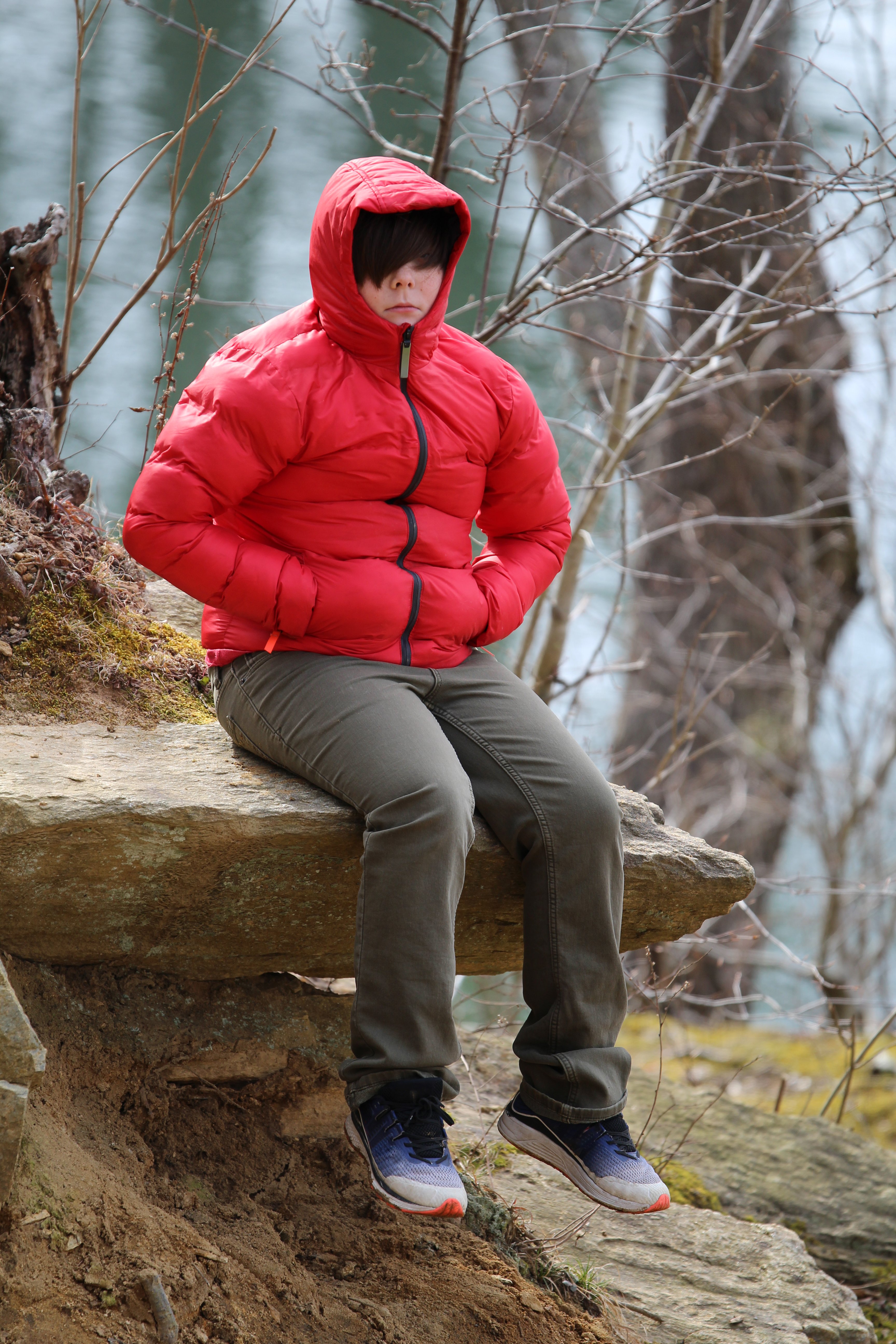 Photo of a young boy in a red coat sitting on a rock in the winter woods. | Photo: Getty Images