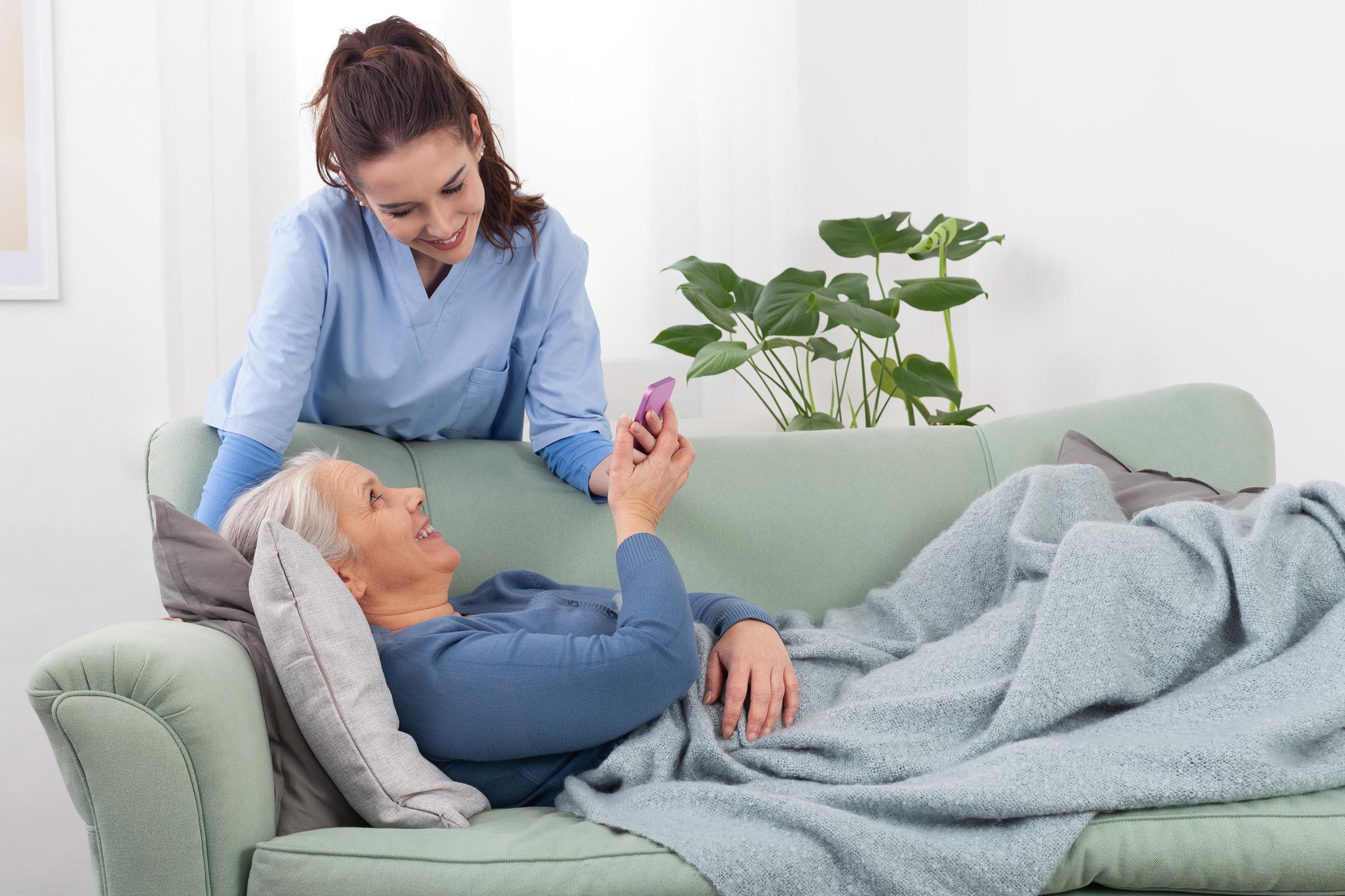 A Nurse Practitioner tending to a senior woman lying on a couch at home | Source: Shutterstock