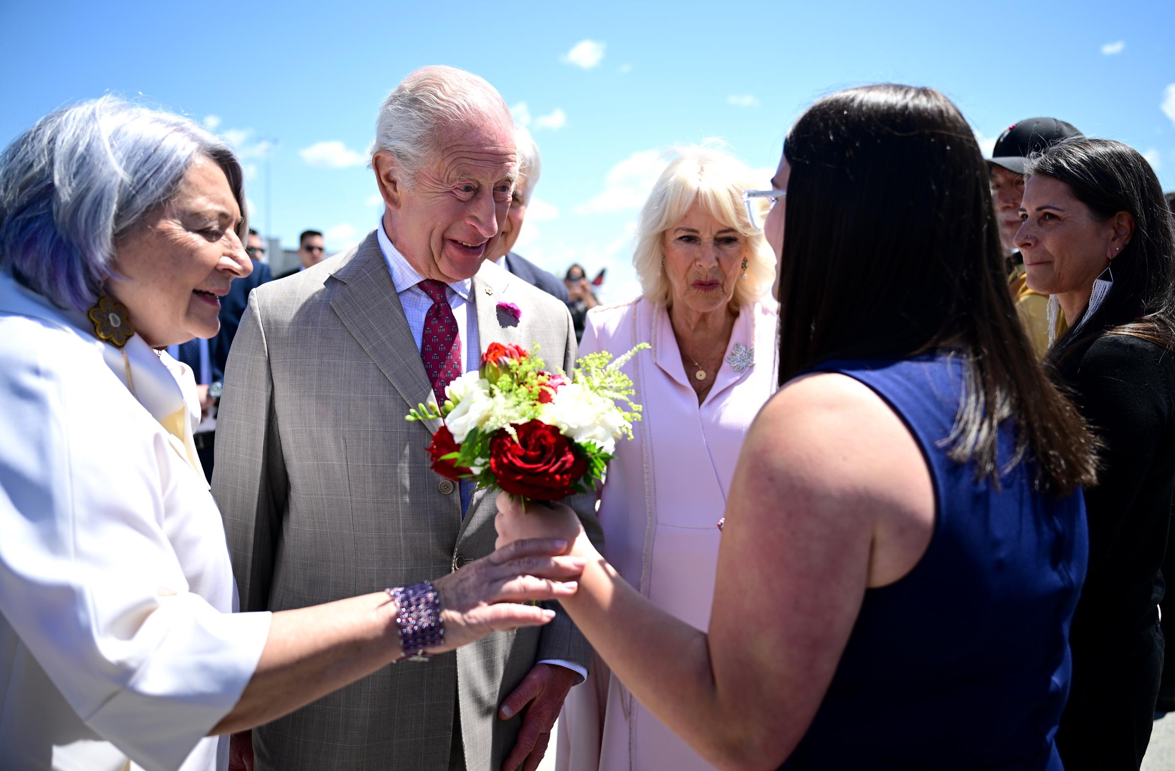 King Charles III and Queen Camilla receive a warm welcome at the airport as a woman presents them with flowers—a gesture symbolizing respect, hospitality, and the spirit of friendship between Canada and the royal family.