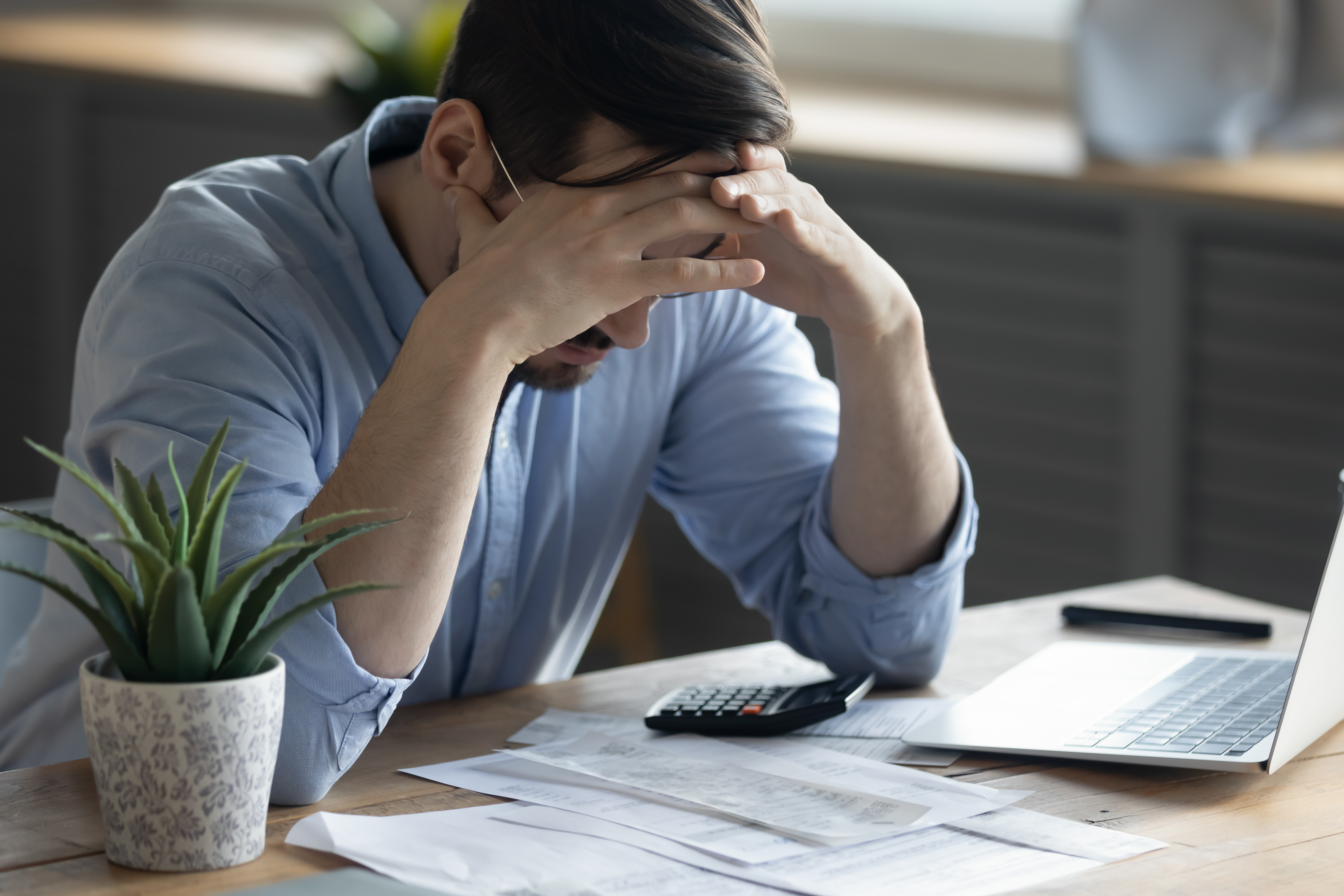 A frustrated man sitting in the office with his hands on his head | Source: Shutterstock