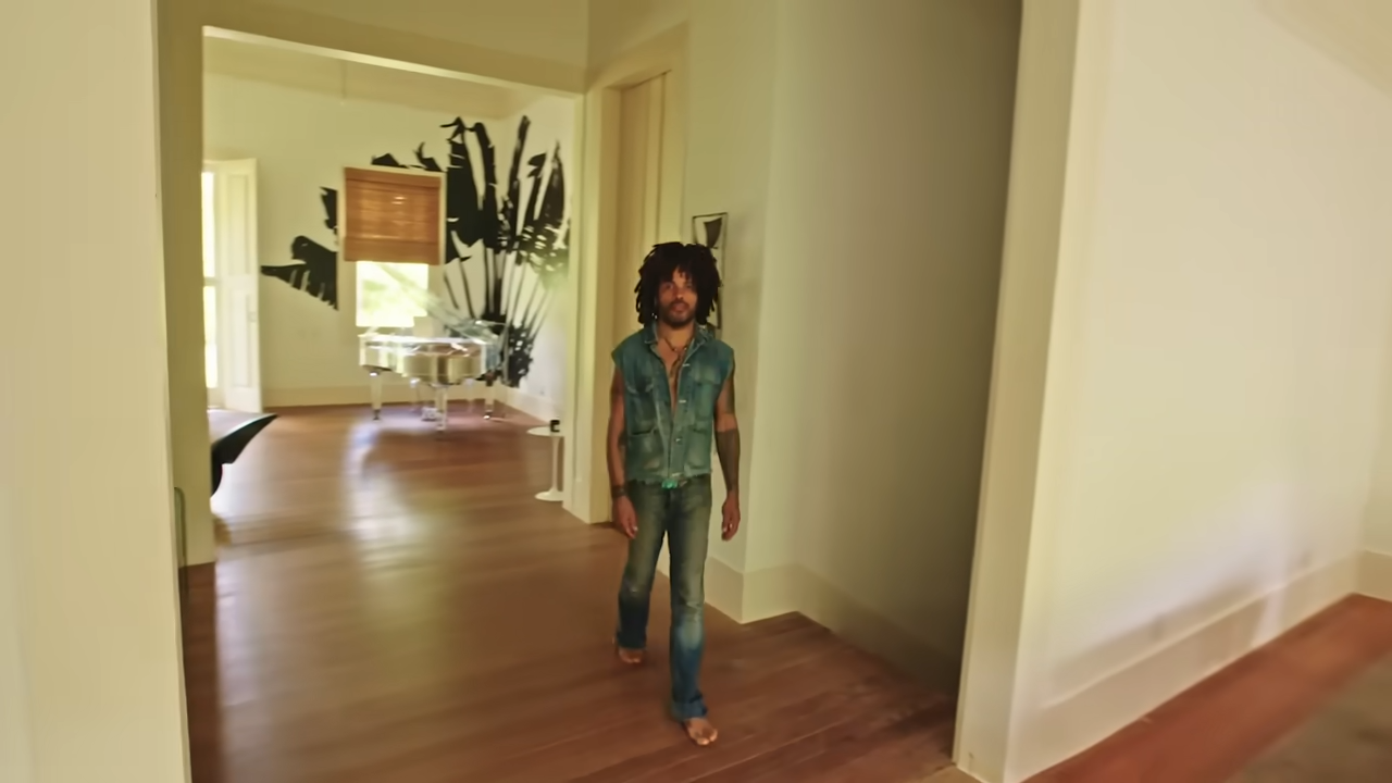 Lenny walks out of a sunlit room featuring his clear Plexiglas grand piano and onto the polished hardwood floors of the farmhouse hallway. | Source: YouTube/@Archdigest