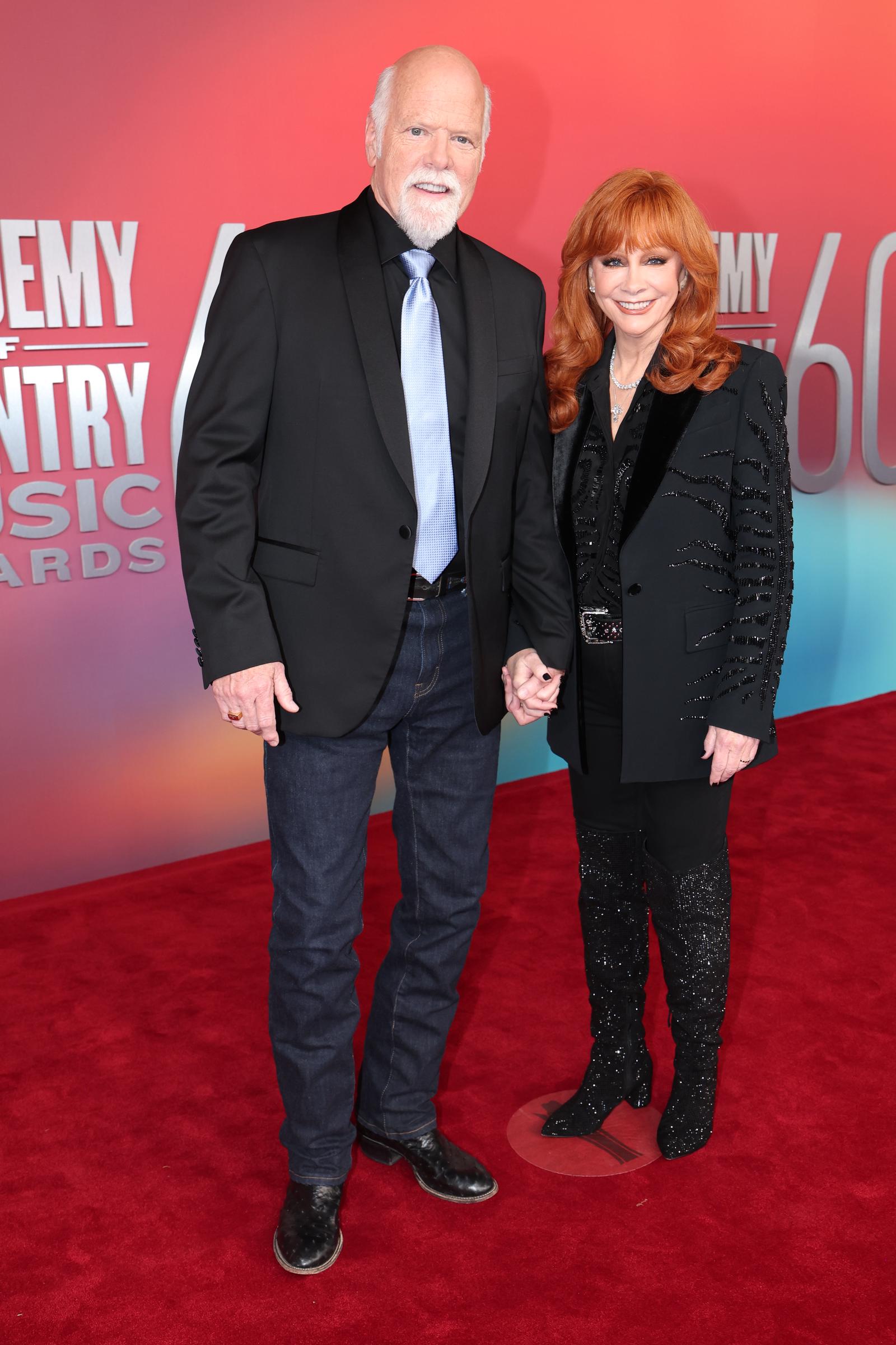 Reba McEntire dazzles in sparkling black boots and a beaded blazer, holding hands with Rex Linn, who keeps it classic in jeans, cowboy boots, and a satin tie