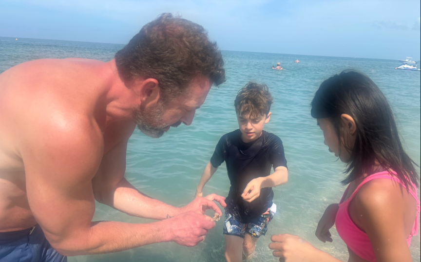 Kristopher Karolkiewicz and two of Amanda "Mandy" Karolkiewicz's children examine a small object together while standing at the edge of the water during the family's spring break vacation. | Source: TikTok/mandykarolk