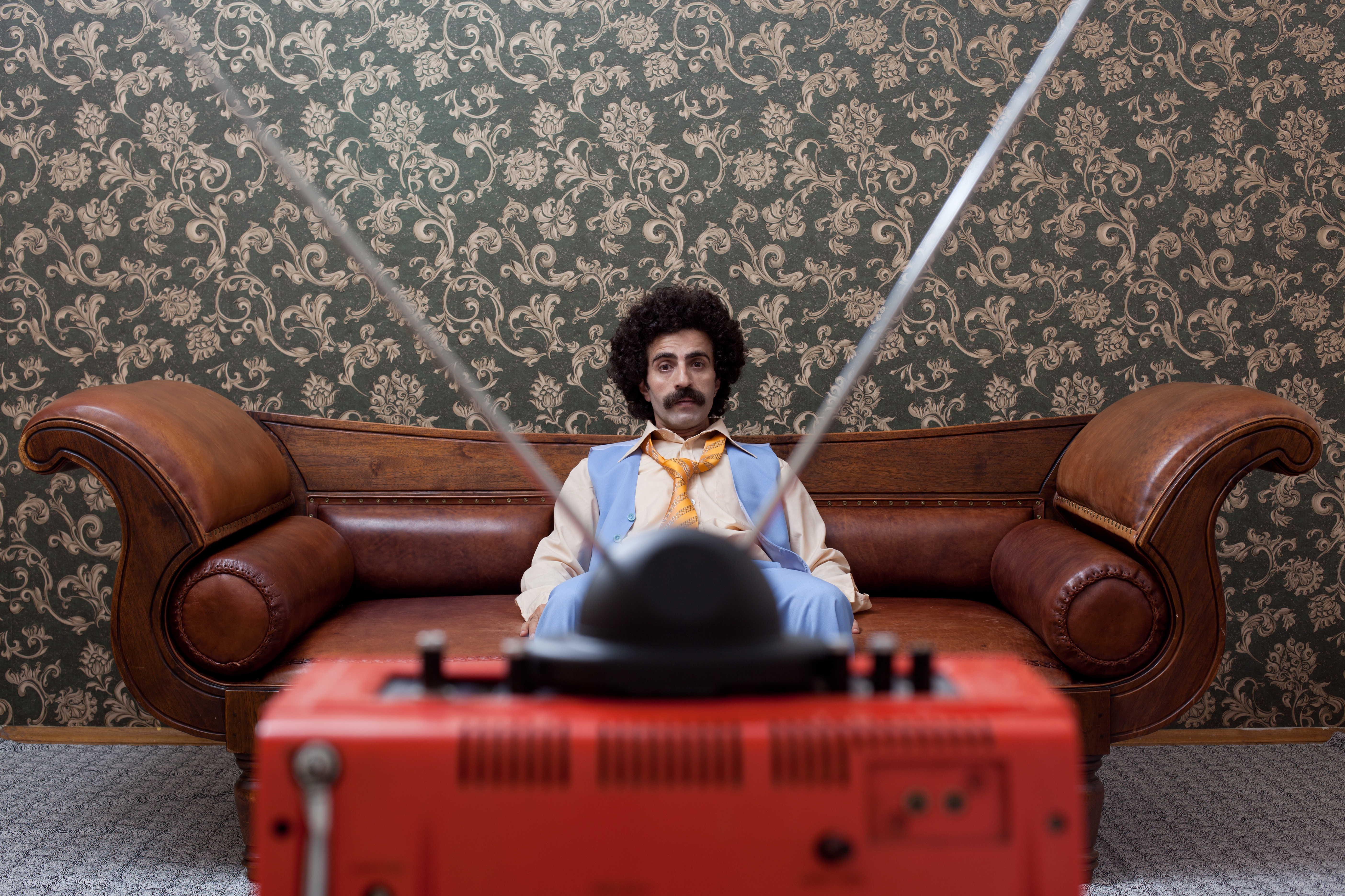 A man sitting in a '70s style living room and watching television. | Source: Getty Images