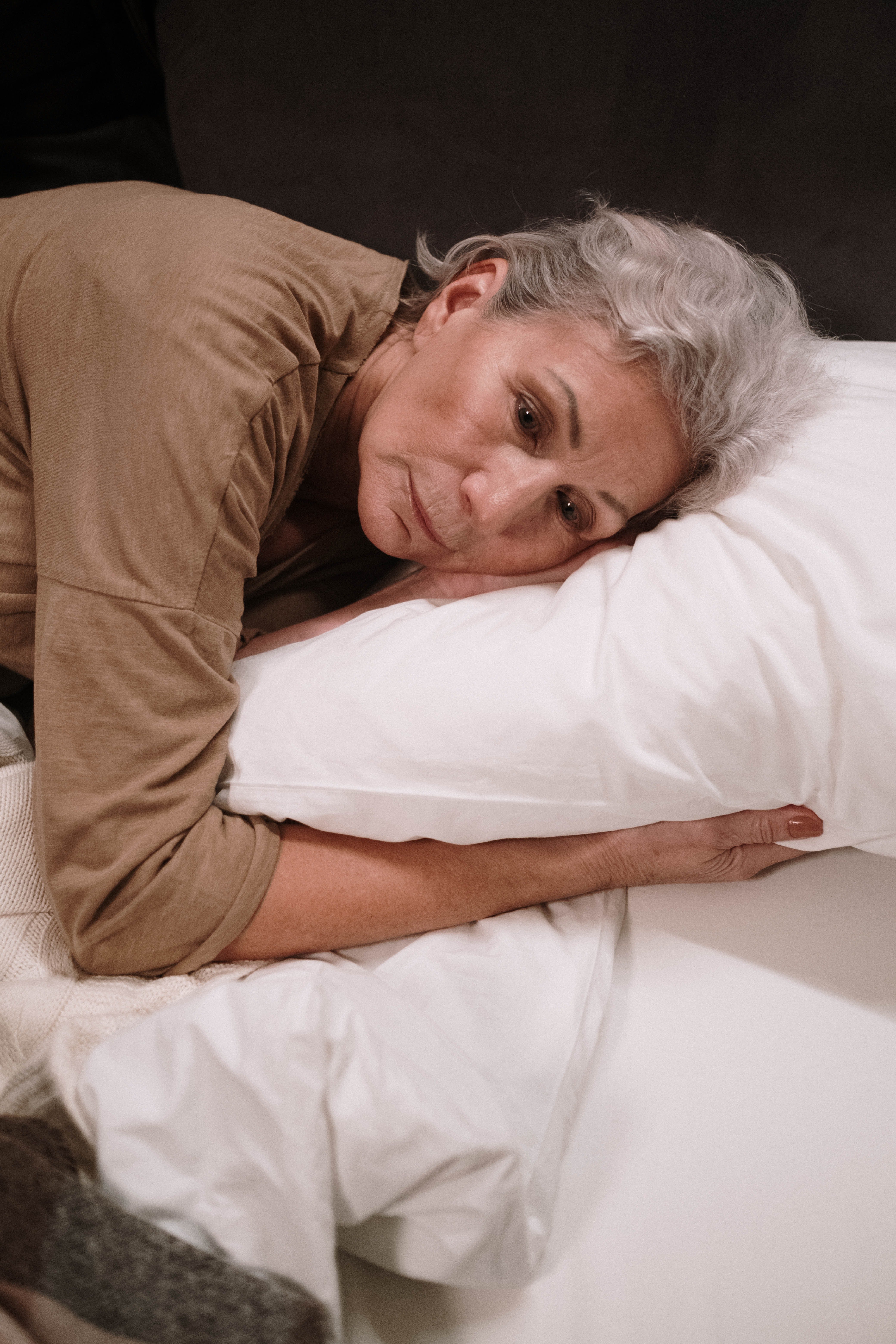 Una mujer mayor con rostro triste recostada en una cama. | Foto: Pexels