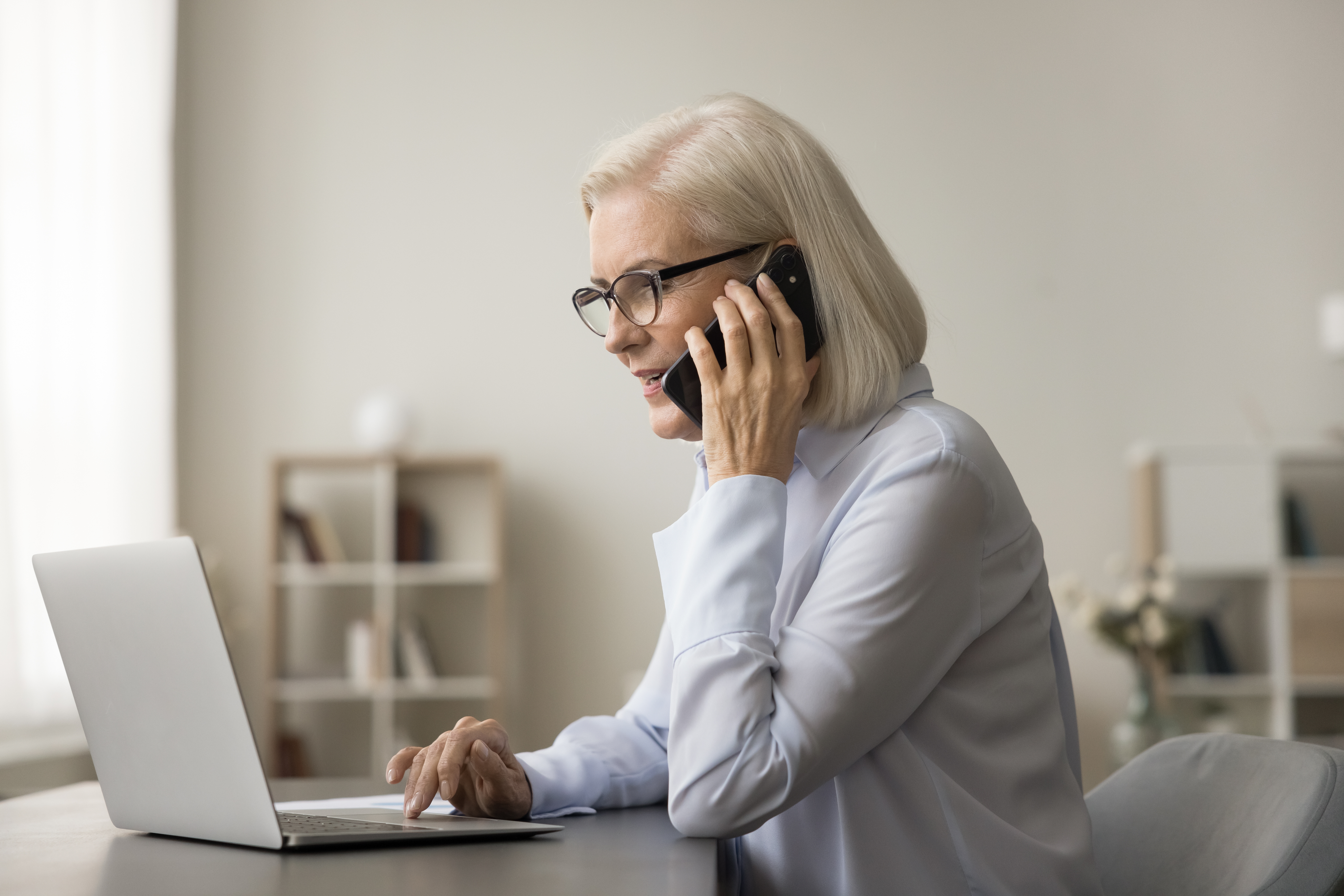 An older woman on the phone while looking at a laptop | Source: Shutterstock