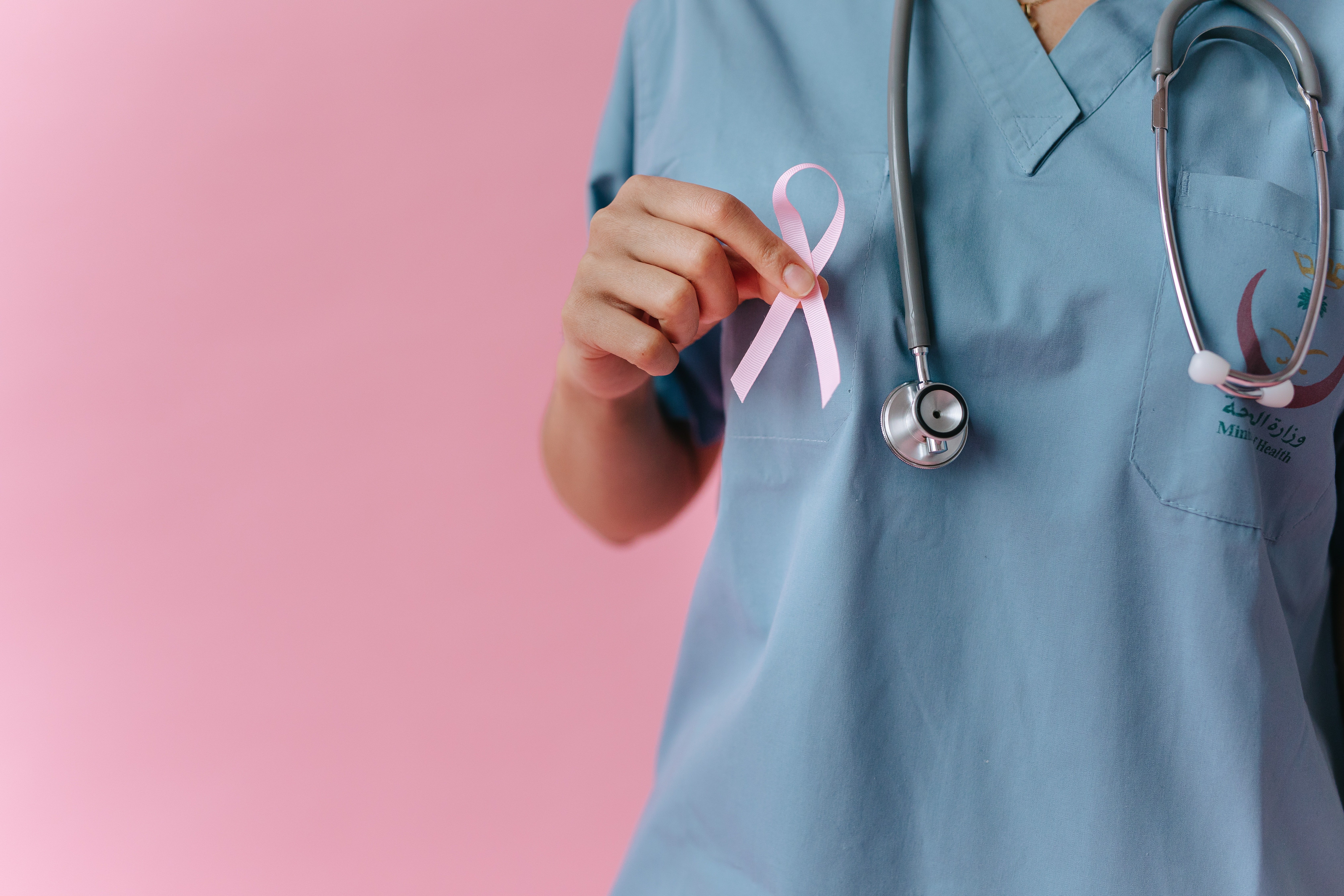Pictured - A photo of an individual wearing scrubs with a stethoscope holding a pink ribbon | Source: Pexels  