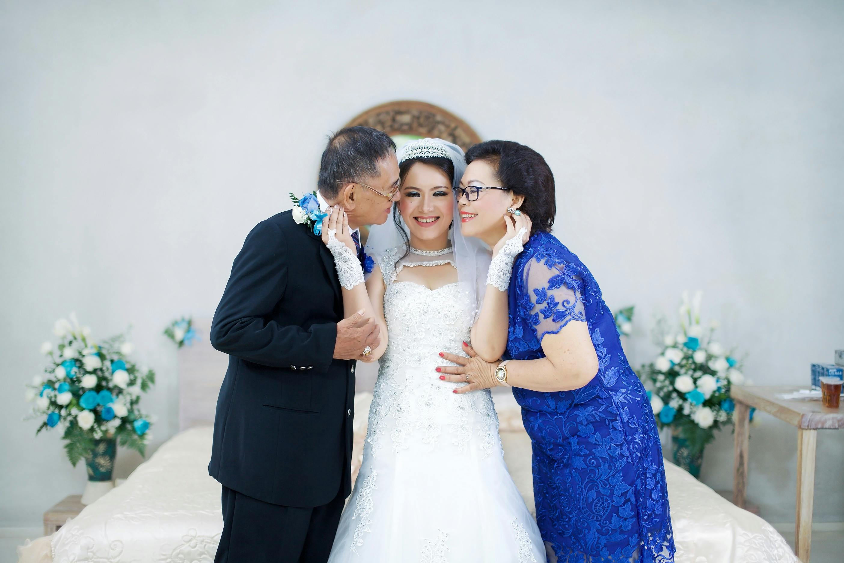 A happy bride posing with her parents on her wedding day | Source: Pexels