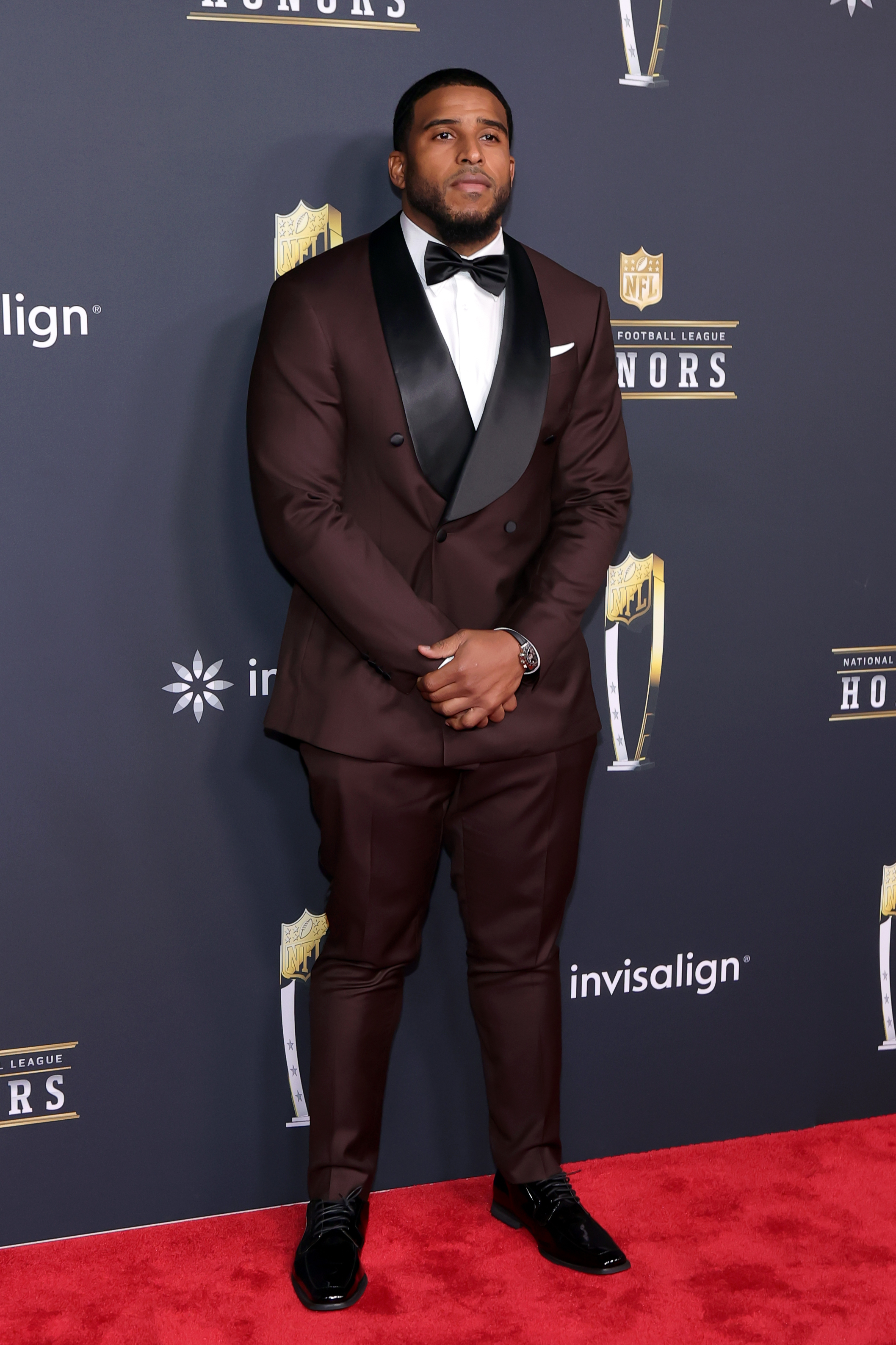 Bobby Wagner opts for a sharp burgundy tuxedo with black lapels, standing poised with hands clasped as he represents the league's elite defensive talent.