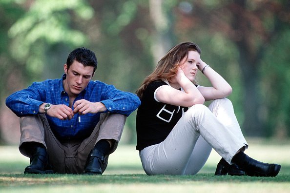 A young couple in casual dress sitting in the park, the woman appears upset and has back turned on the man | Photo: Getty Images