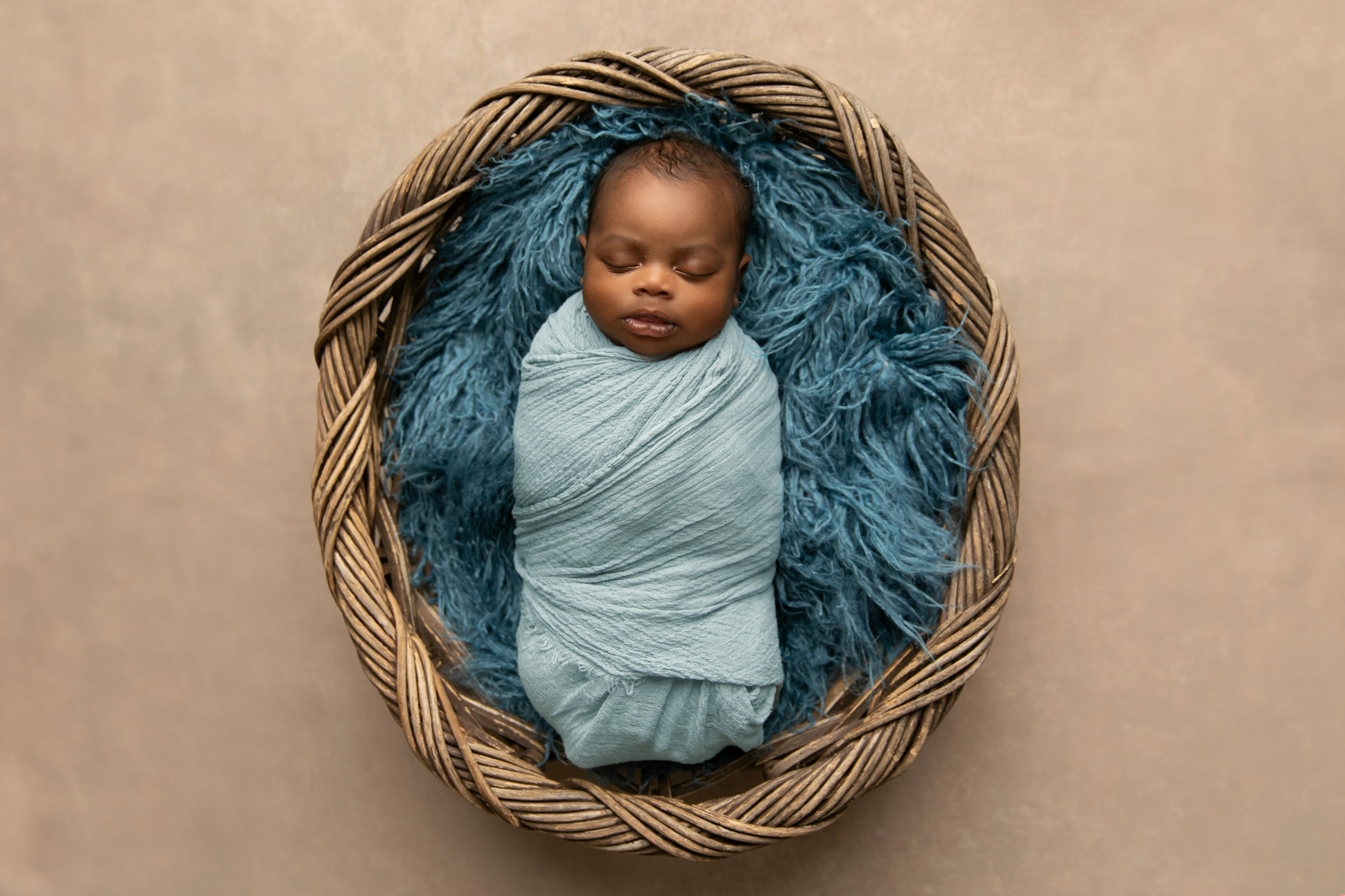 Ein afroamerikanischer neugeborener Junge, der in einem Korb auf einem blauen Teppich liegt und in eine Decke gewickelt ist | Quelle: Shutterstock