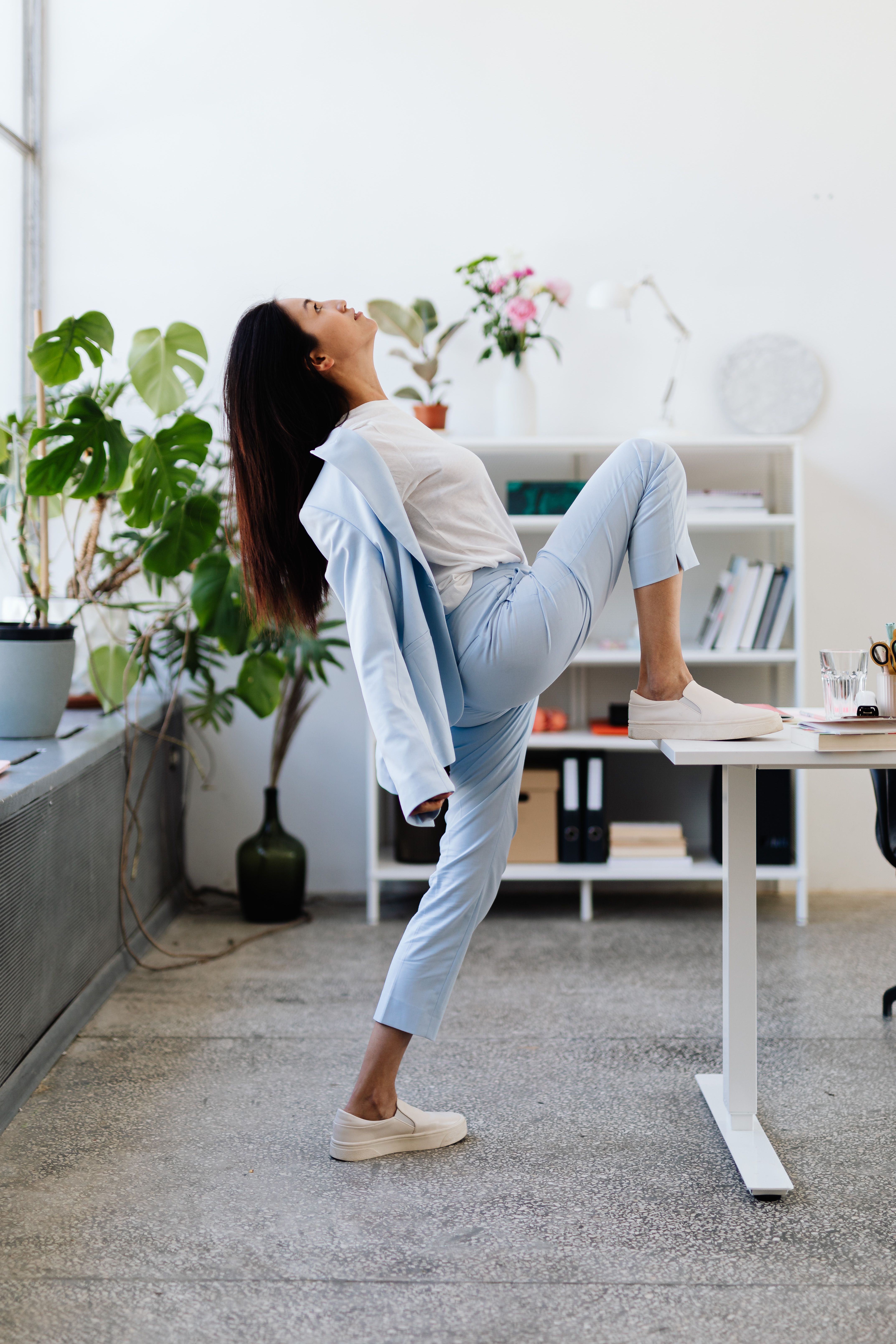 A woman stretches her leg on a desk during a work break. | Source: Pexels