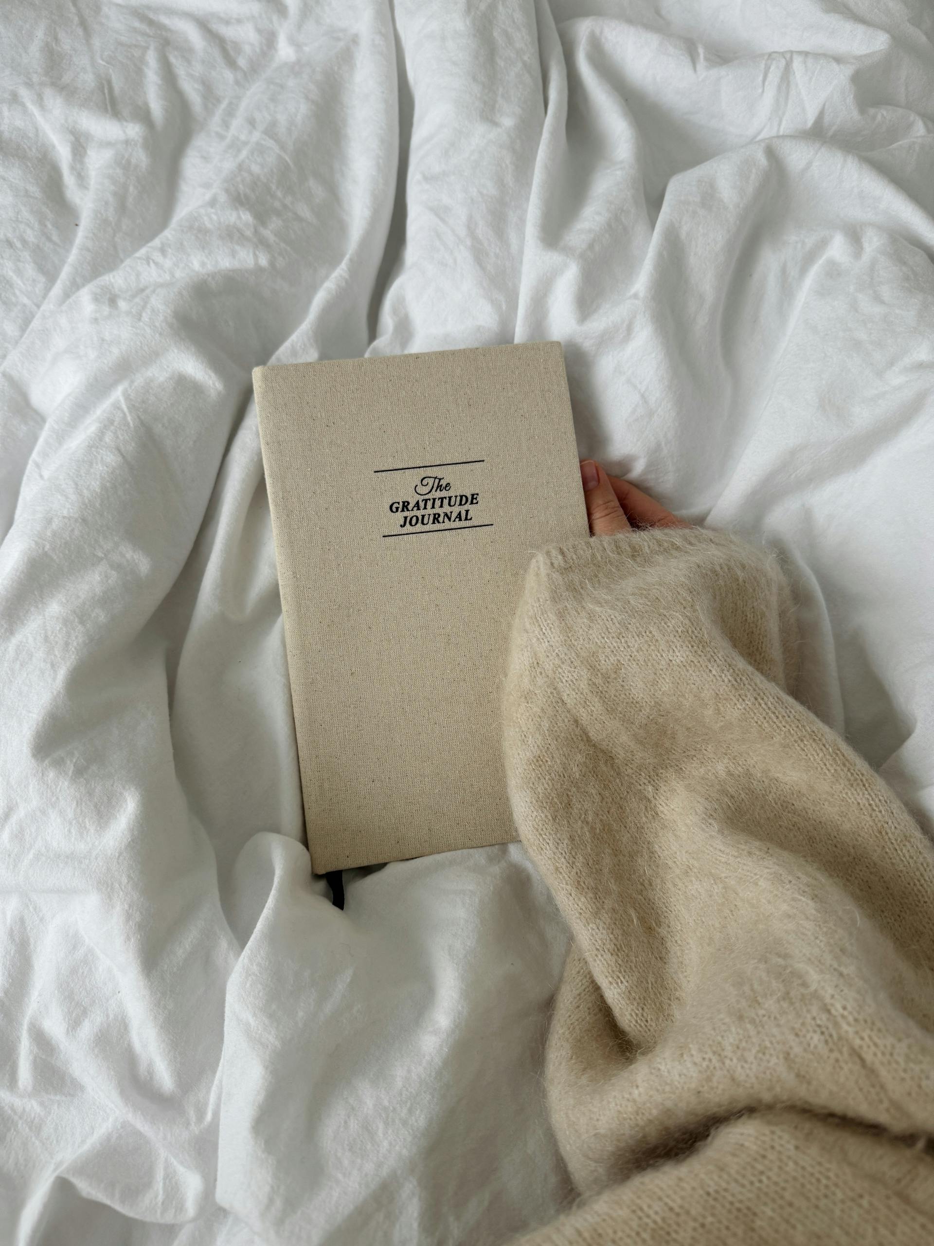 A closeup shot of a person holding a gratitude journal in bed | Source: Pexels