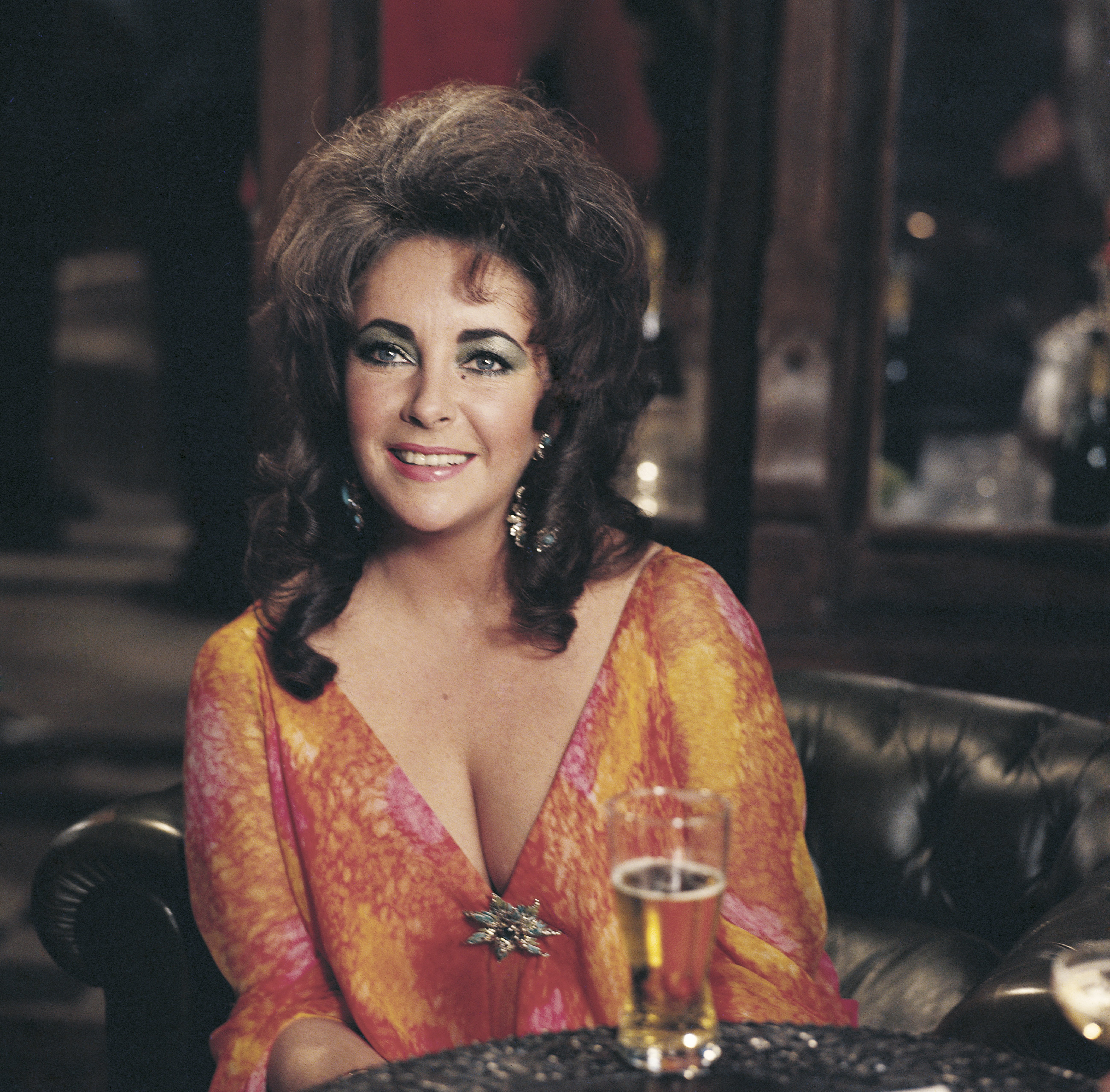 British-born American actress Elizabeth Taylor smiling wearing a low-necked dress, in front of a glass of beer. 1973. | Source: Getty Images