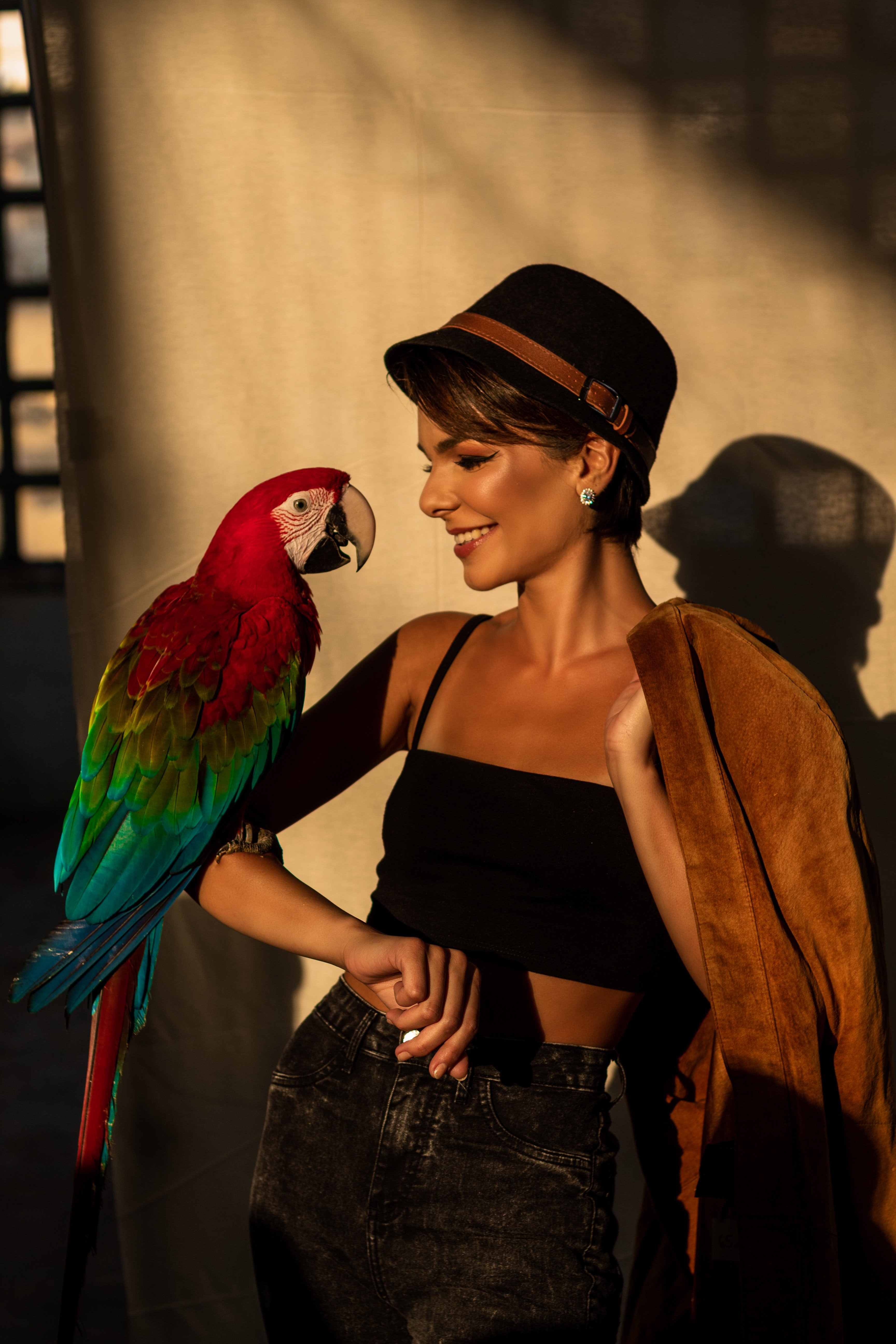 A big colorful parrot sitting on the arm of a woman wearing a hat. | Pexels/ Luiz Fernando