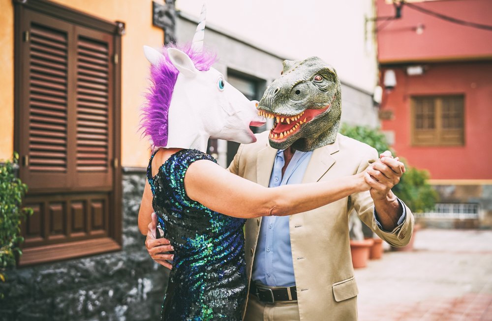 Pareja excéntrica bailando con máscaras de unicornio y de dinosaurio. | Foto: Shutterstock Pareja excéntrica bailando con máscaras de unicornio y de dinosaurio. | Foto: Shutterstock