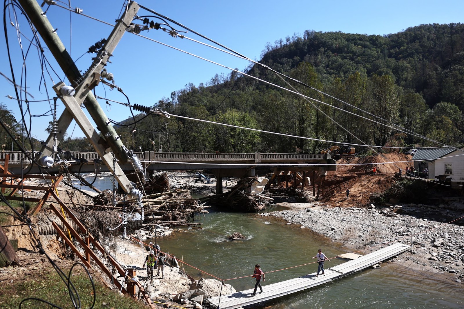 People walking across a makeshift bridge as a damaged bridge is repaired in the aftermath of Hurricane Helene flooding on October 8, 2024, in Bat Cave, North Carolina. | Source: Getty Images