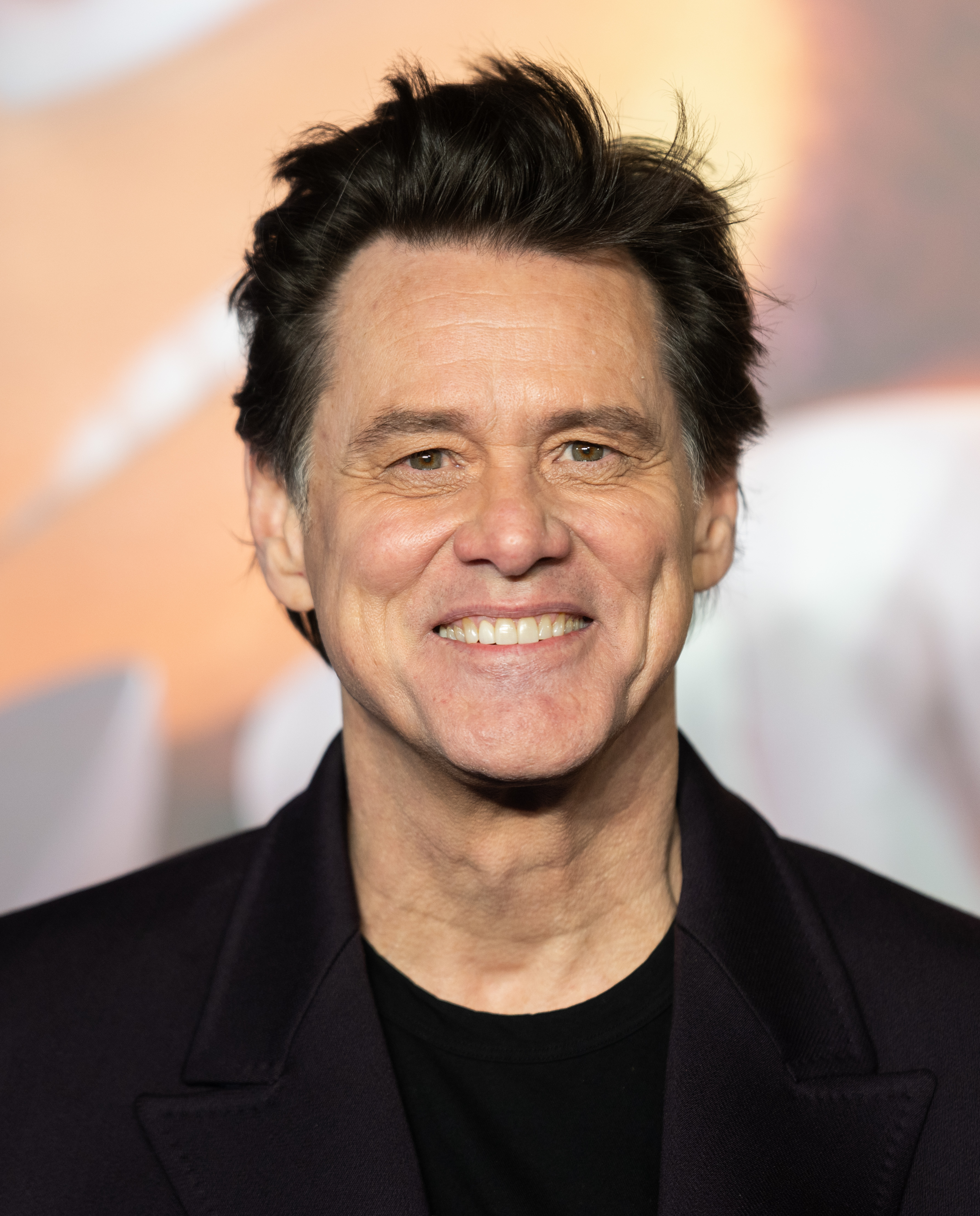 Smiling warmly for the cameras, Jim Carrey appears in a sleek dark ensemble with softly tousled hair. The blurred premiere backdrop casts a warm glow that frames his unmistakable grin. He attends the "Sonic The Hedgehog 3" UK Premiere at Cineworld Leicester Square.