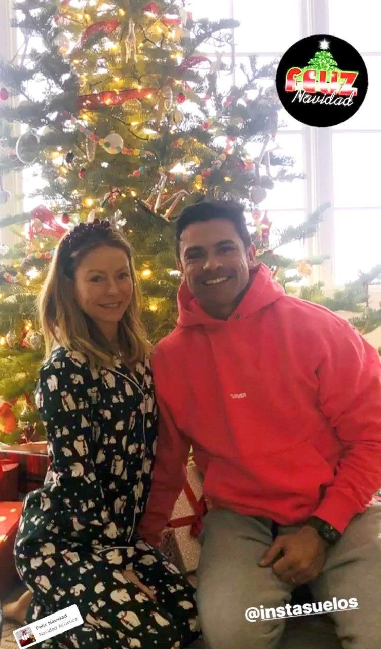 Kelly Ripa and husband, Mark Consuelos posing in front of a Christmas tree | Photo: Instagram/instasuelos