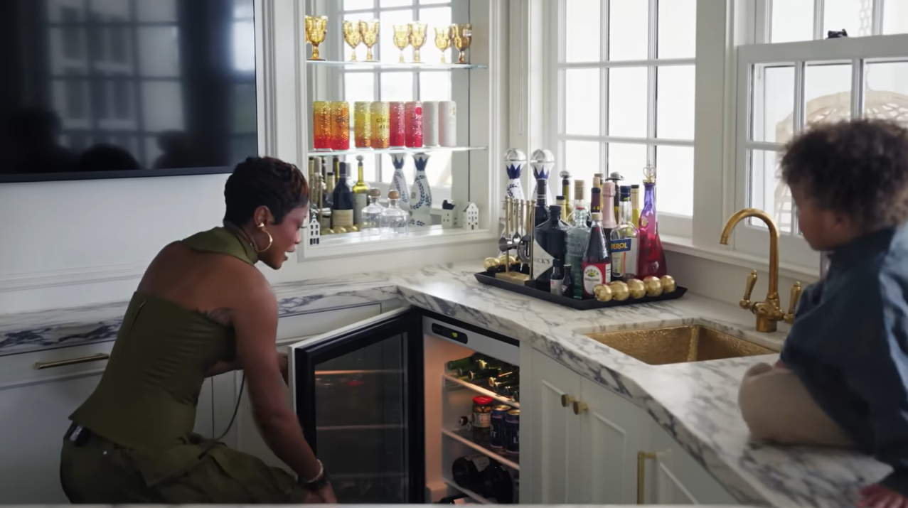 Palmer crouches down to raid her built-in mini fridge under the marble bar counter while little Leo supervises. | Source: YouTube/@Archdigest