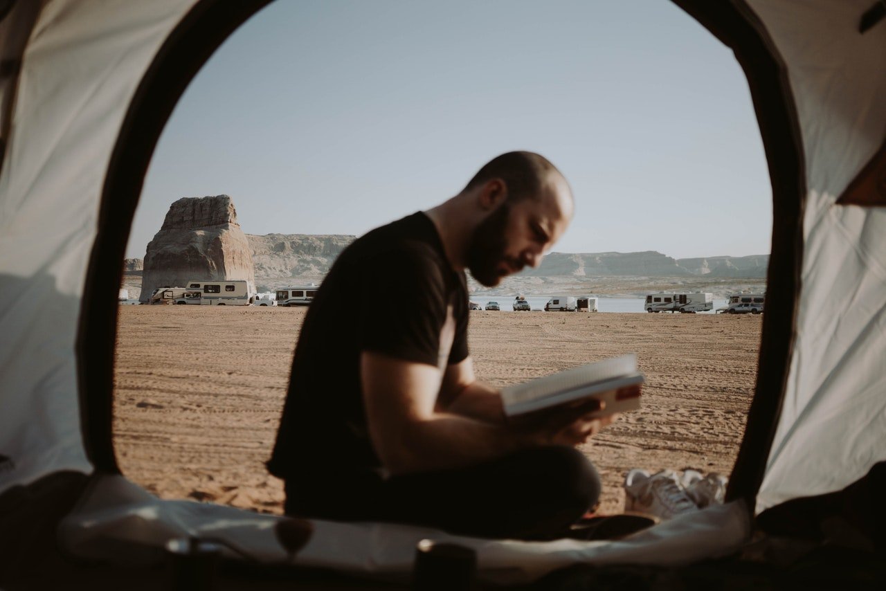 Photo of man reading a book in a tent | Photo: Pexels