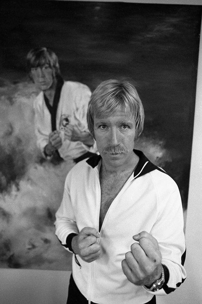 Chuck Norris posing in front of a  poster on the wall of his home in 1978 in Palos Verdes, California | Photo: Nik Wheeler/Corbis via Getty Images