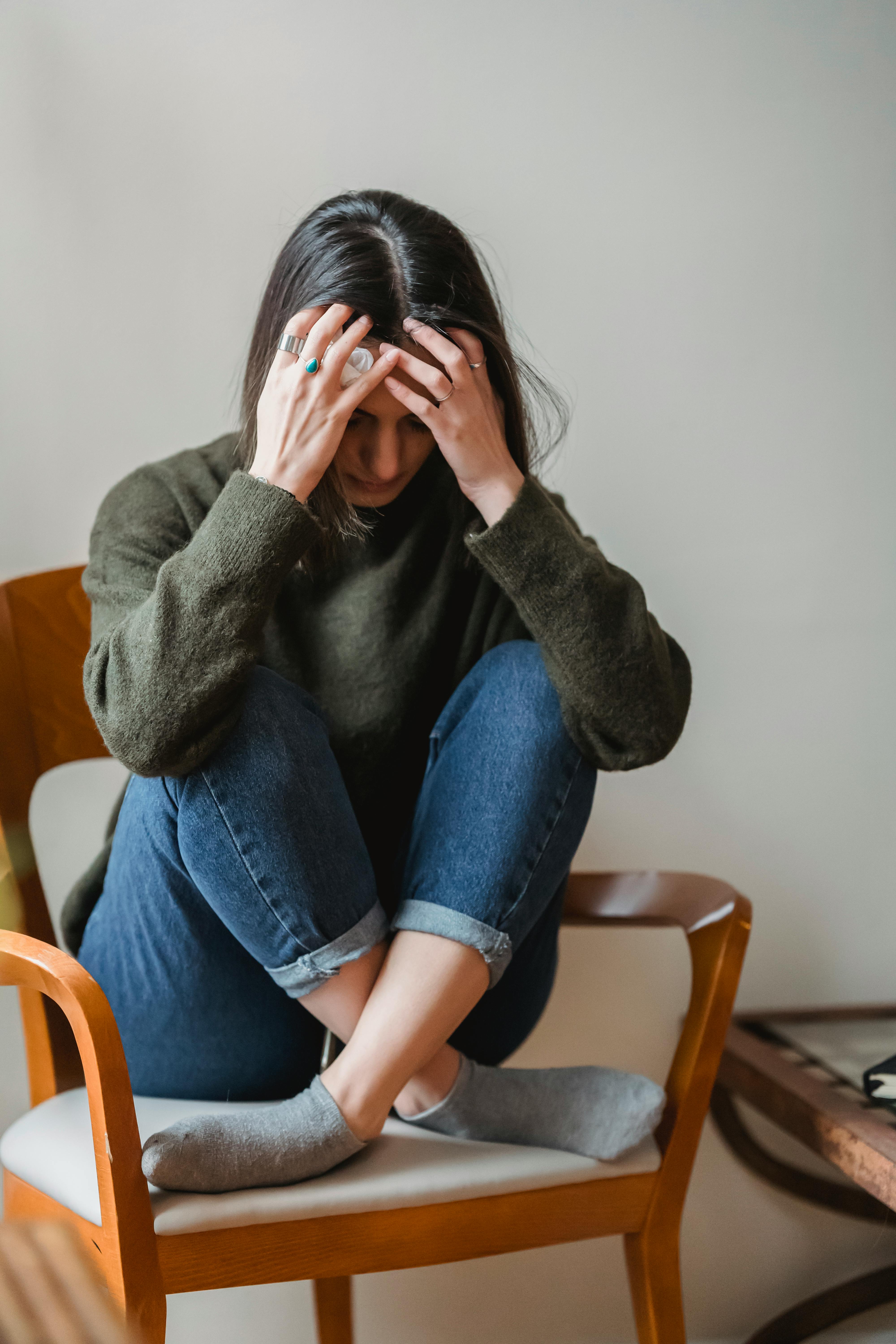 A young woman grabbing her head while sitting on a chair | Source: Pexels