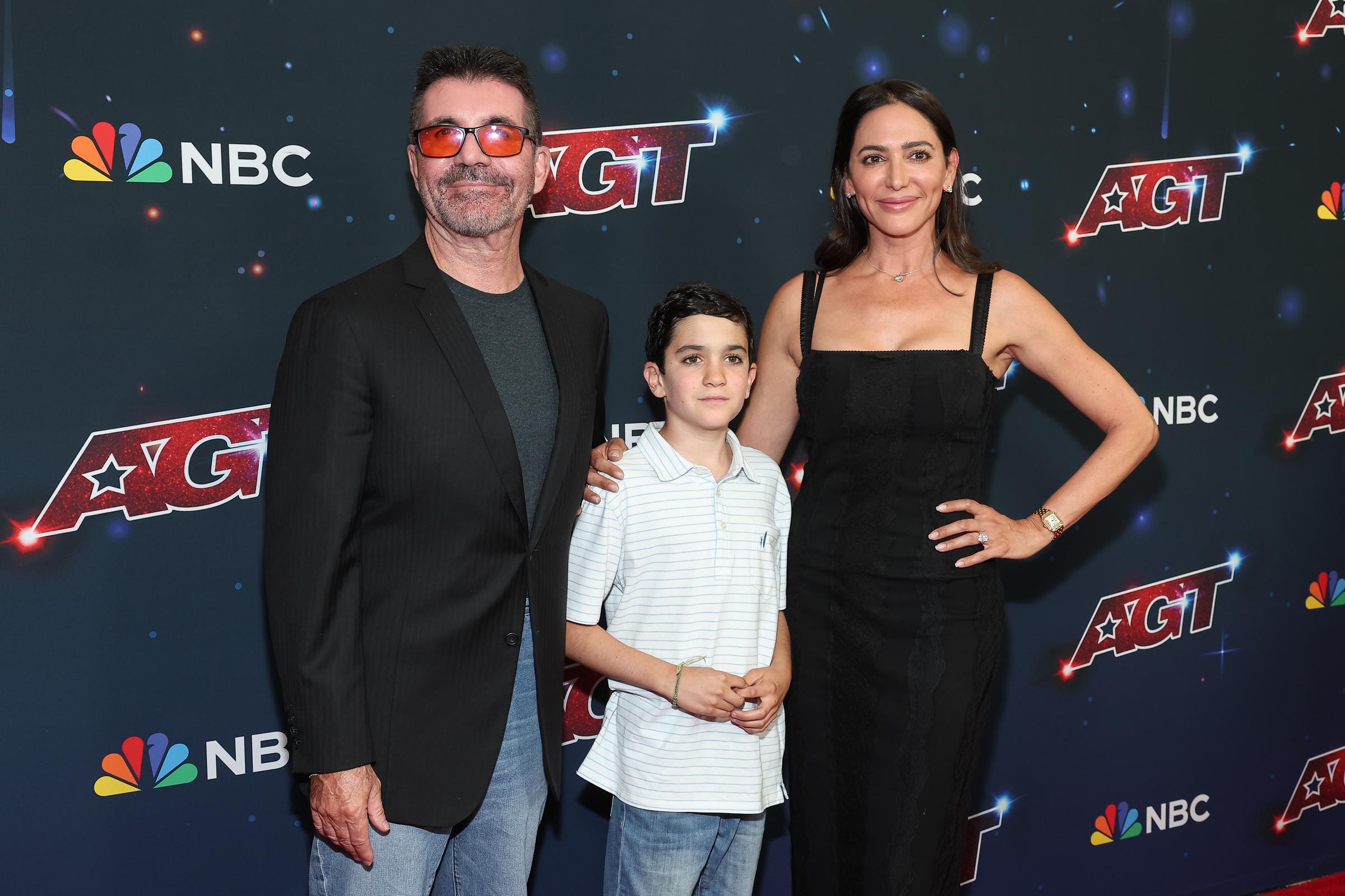 Eric, standing between his parents Simon Cowell and Lauren Silverman, looks ahead at the "America’s Got Talent Season" 18 Finale held at the Hotel Dena in Pasadena, California. The family appears poised and united as they mark the occasion together.
