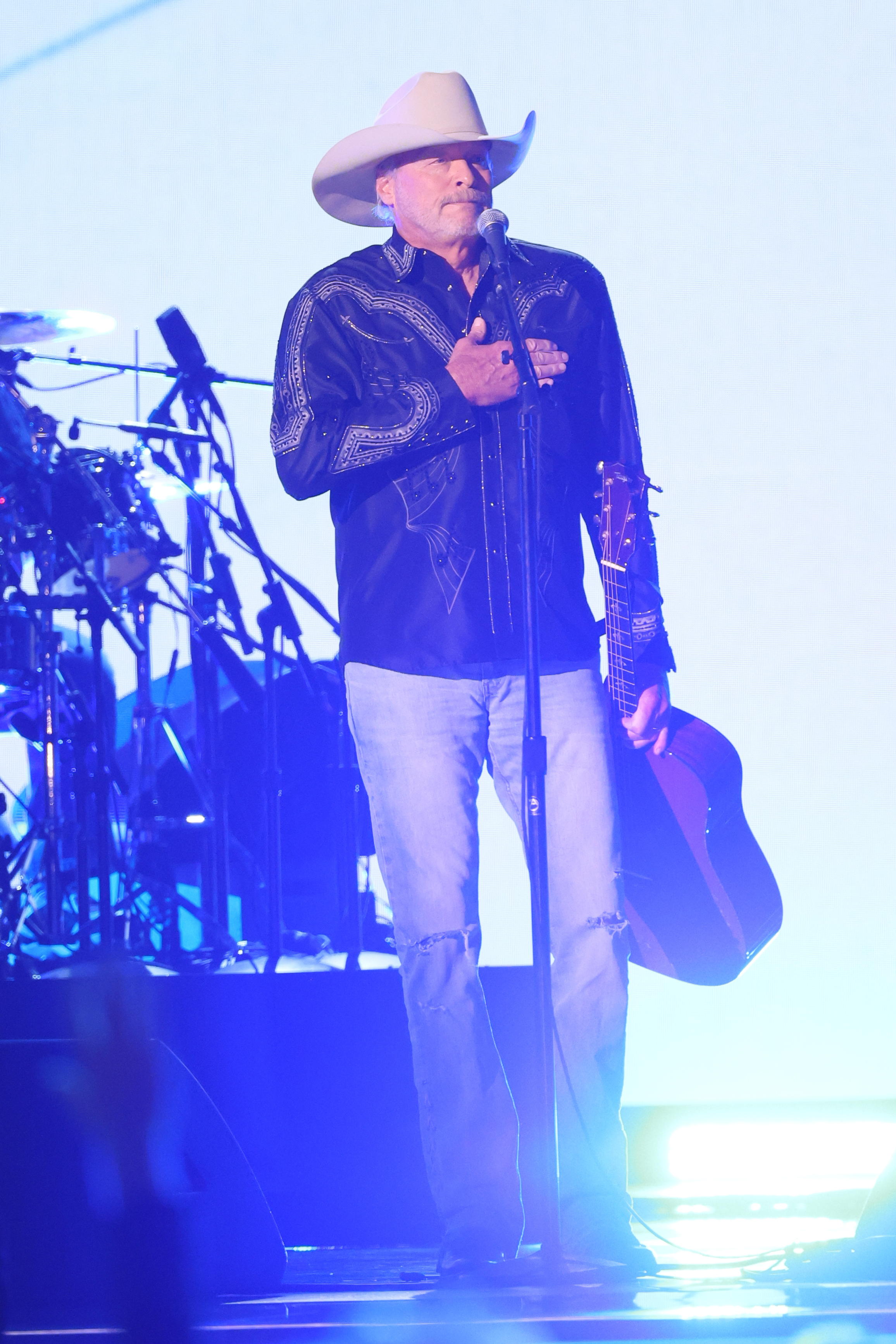 Alan Jackson performs onstage during the 60th ACM Awards at The Star in Frisco, Texas. Donning a white cowboy hat and embroidered black shirt, he plays guitar during his heartfelt set under moody purple stage lighting.