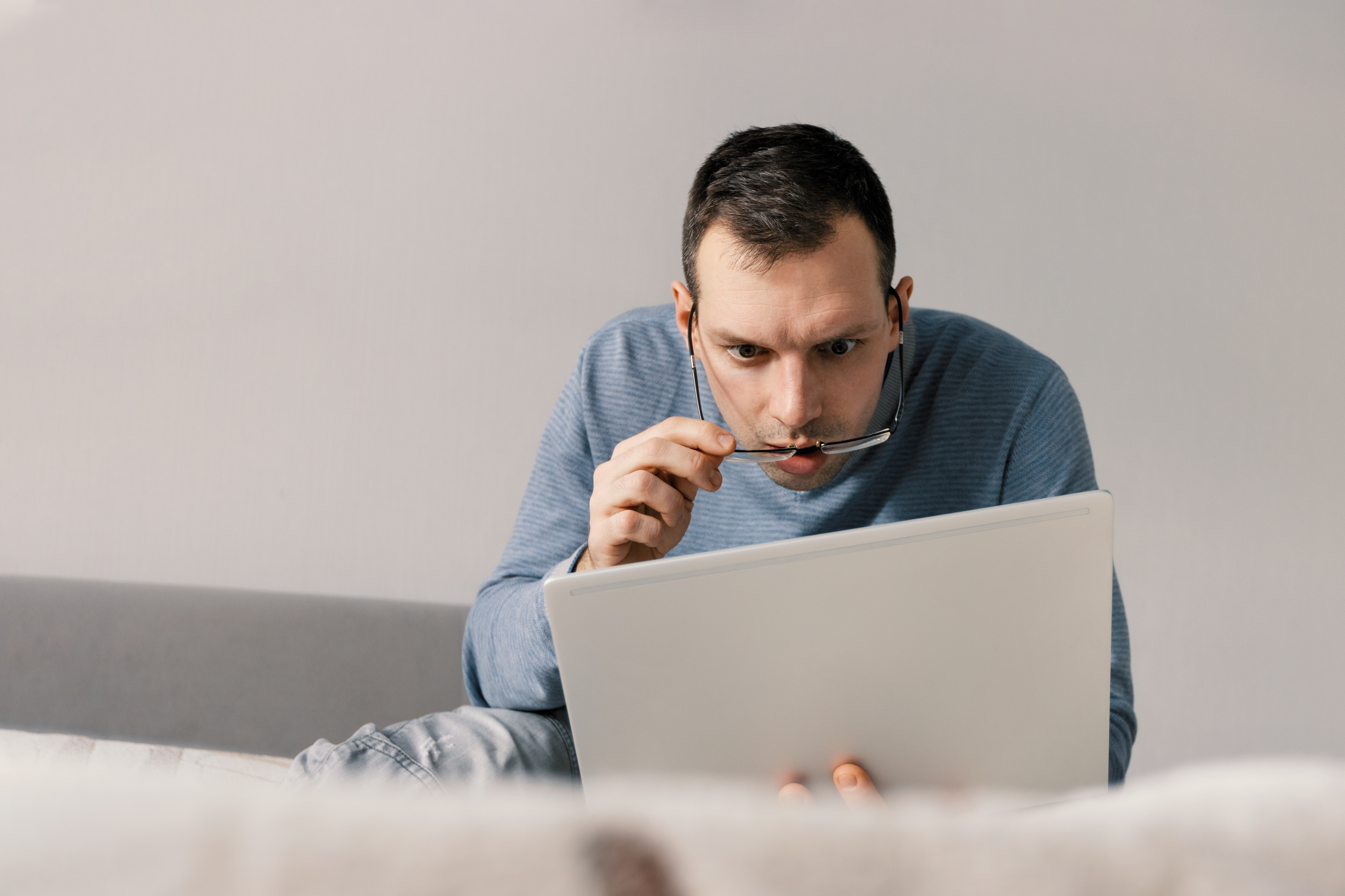 Shocked astonished man in eyeglasses looking at laptop screen while sitting on sofa at home. Facial expression - wow | Source: Getty Images