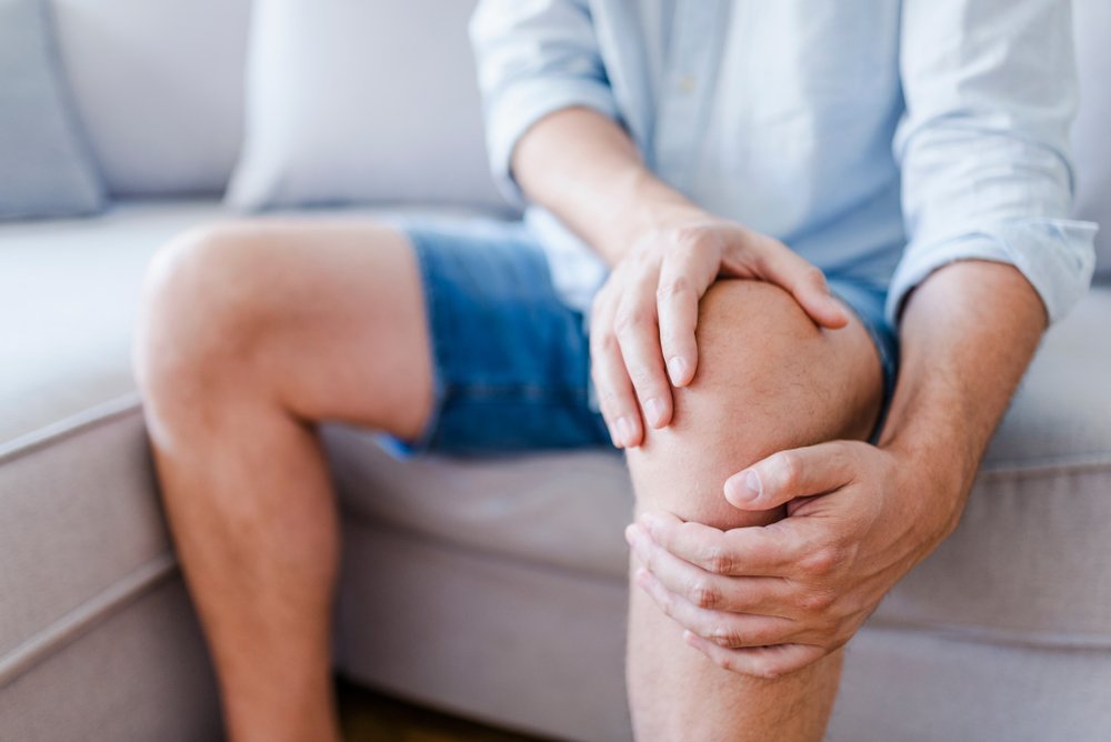 Hombre que sufre de dolor de rodilla sentado en un sofá. Fuente: Shutterstock