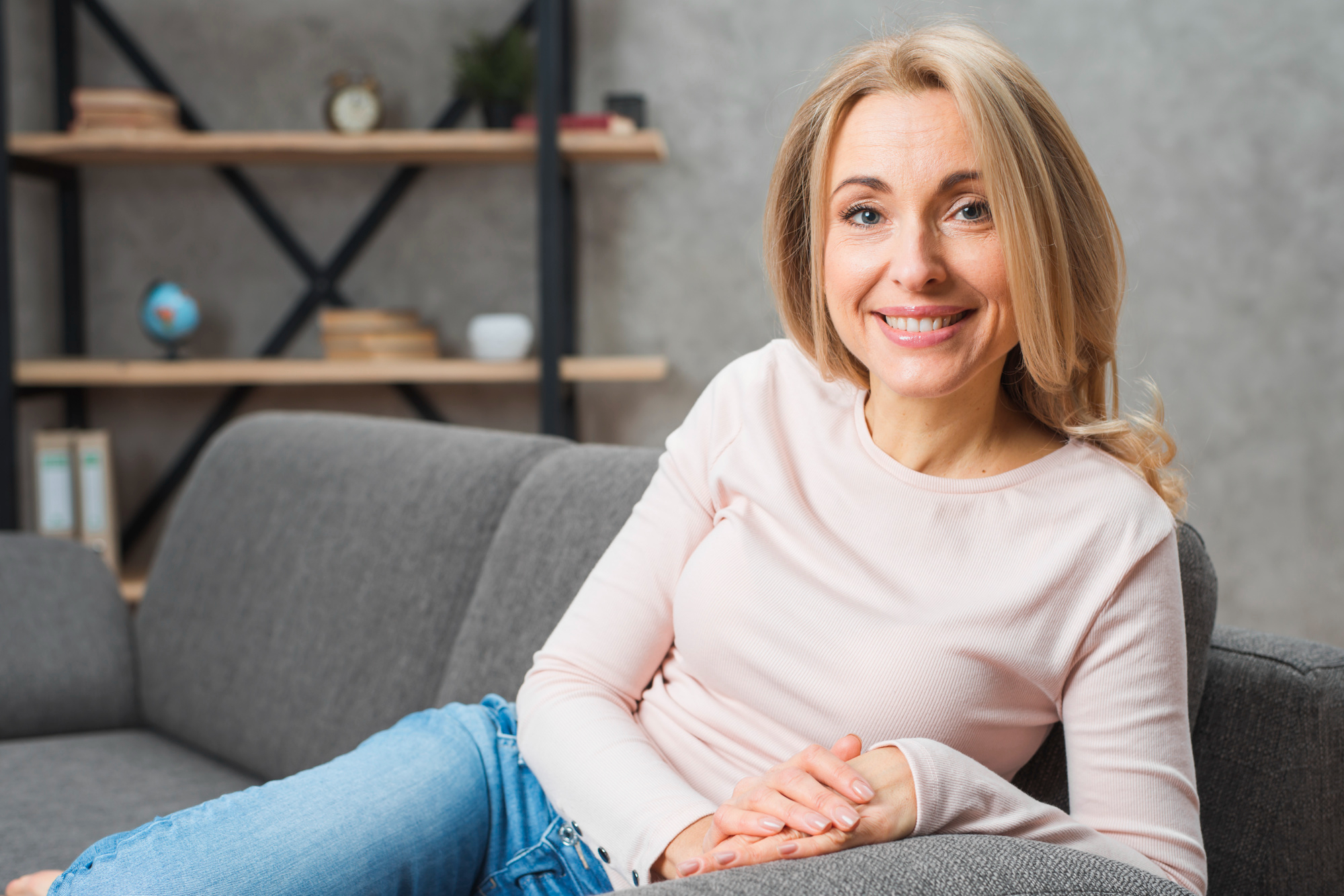 A smiling blonde woman sitting on a sofa looking at the camera | Source: Freepik