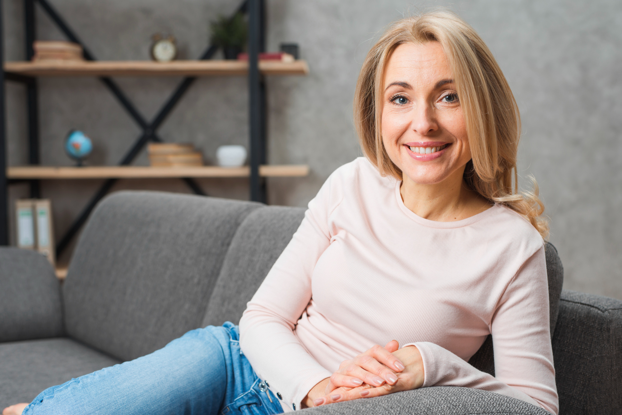 Una mujer rubia sonriente sentada en un sofá mirando a la cámara | Fuente: Freepik