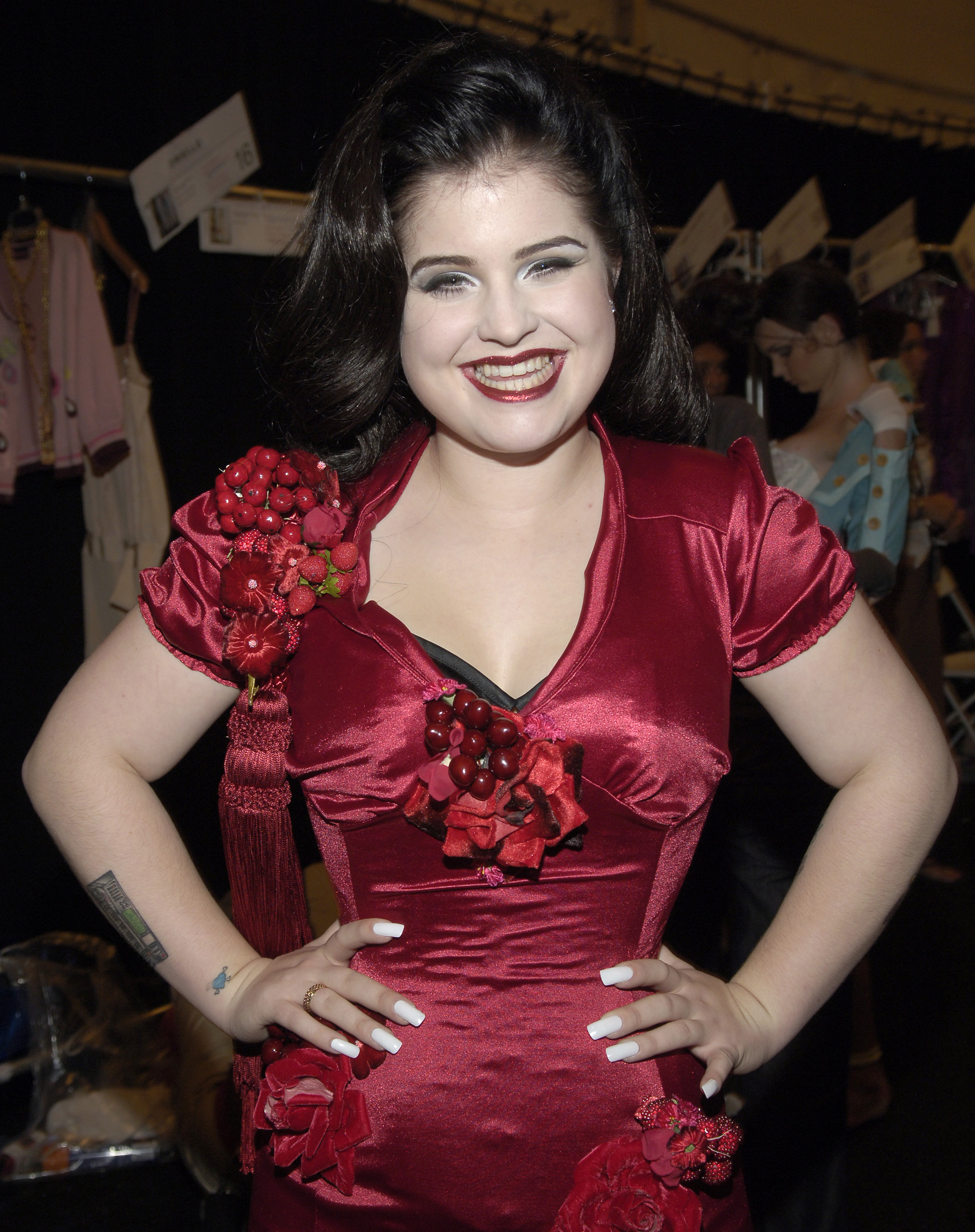 Stepping backstage at Heatherette during Olympus Fashion Week Spring 2006, on 16 September 2005, Kelly stuns in a playful red satin number, dripping in floral and berry embellishments — a bold glimpse of her fearless fashion spirit.