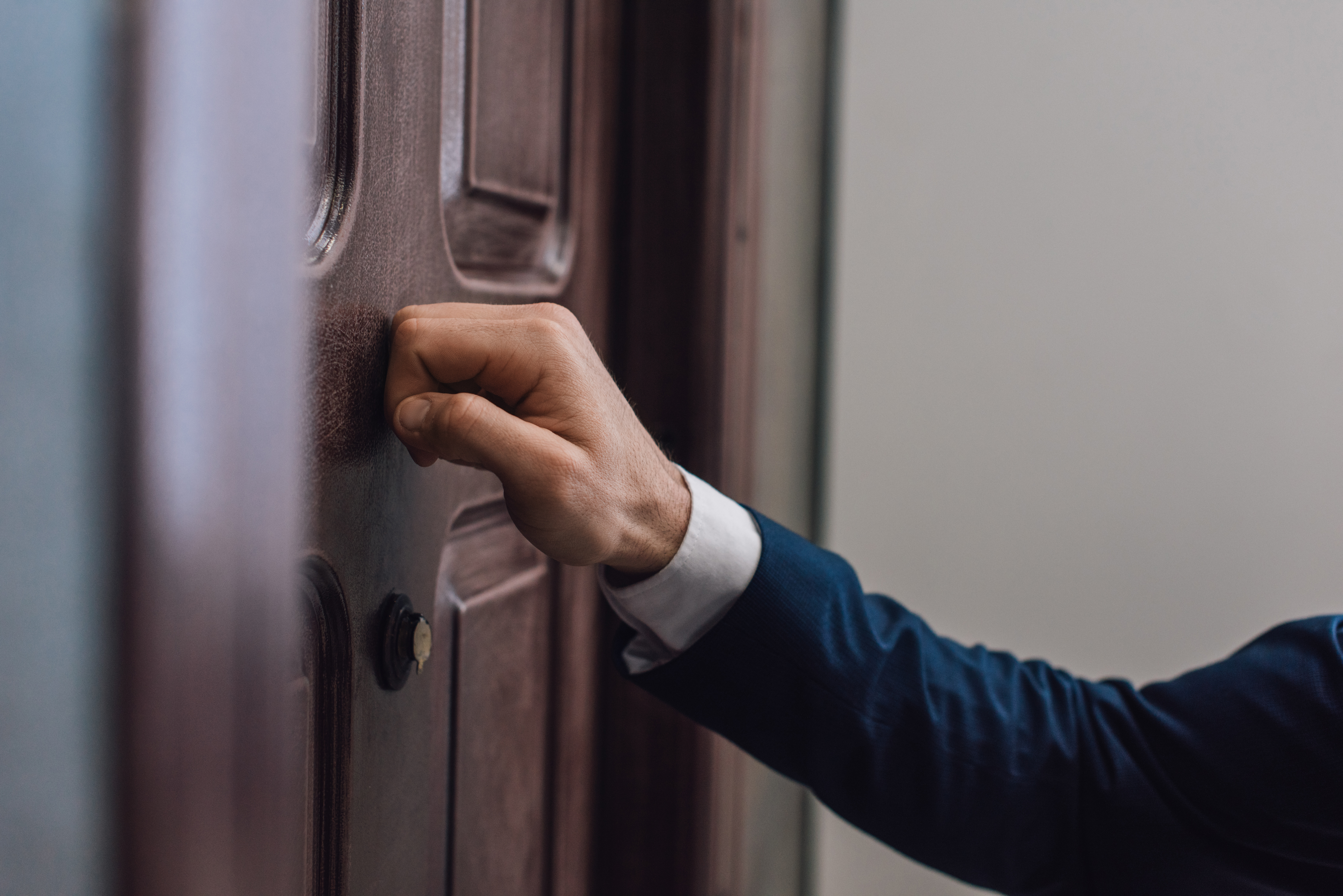 Cropped view of man knocking on door with hand. | Source: Shutterstock