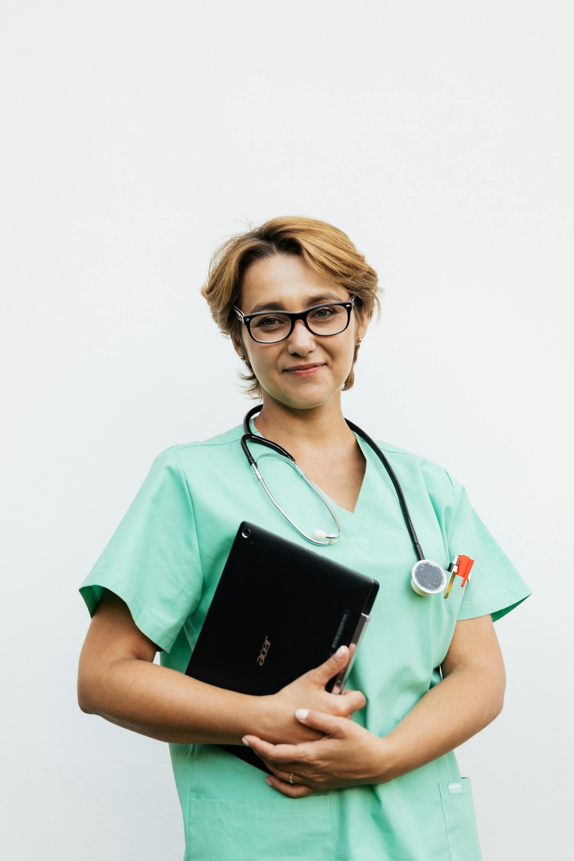A nurse in green scrubs smiling while holding her laptop | Source: Pexels