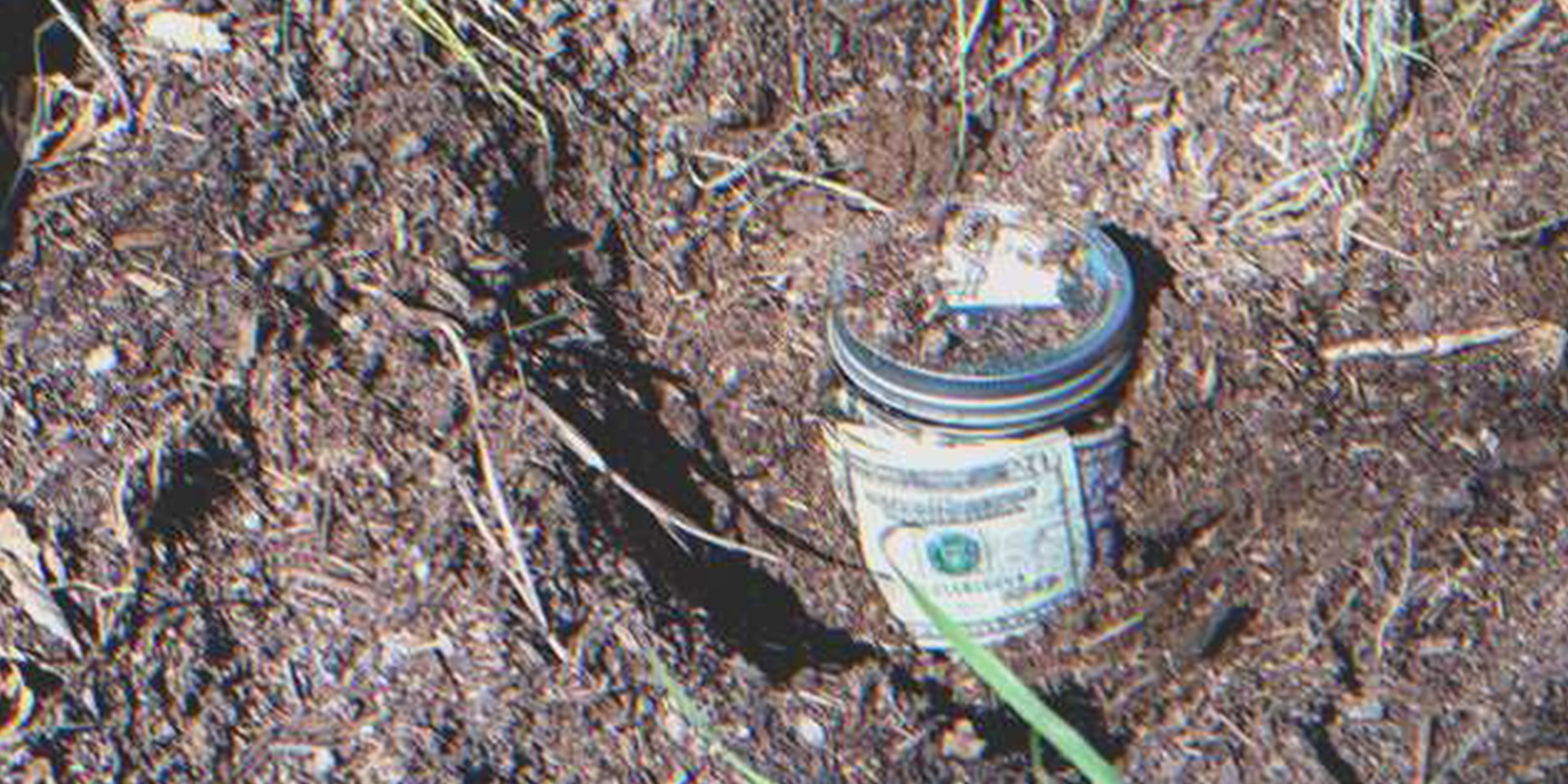 Una jarra de vidrio llena de billetes enterrada en el suelo | Foto: Shutterstock