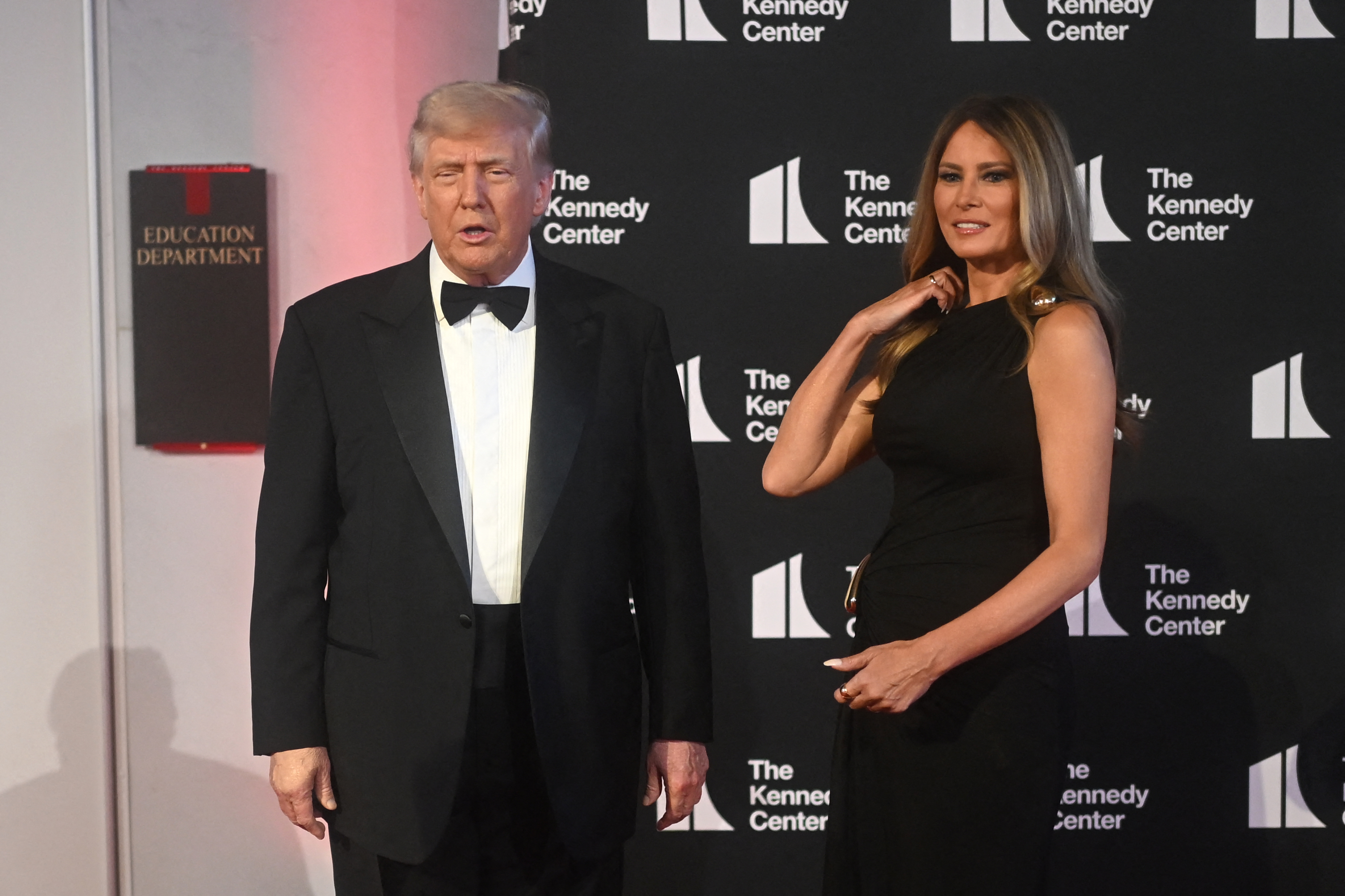 The couple stands on the red carpet, looking like they're waiting for the press to tell them what to do next. Donald's tux looks tailor-made, and his formal stance matches it well. Melania brings a hand up to her hair; this small adjustment makes onlookers notice the sleek design and gold details of her gown.