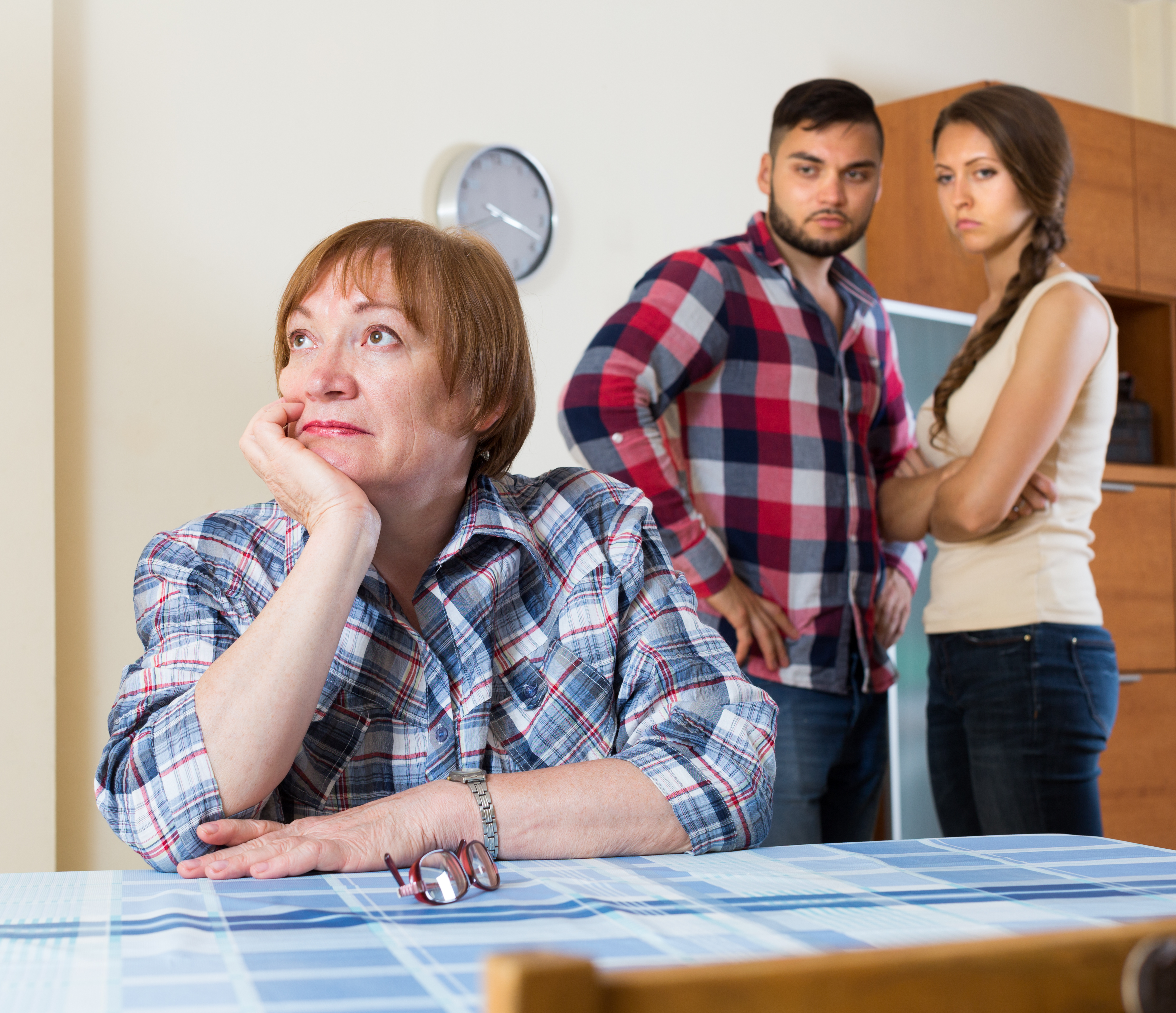 An upset couple standing in the background looking at a smug older woman | Source: Shutterstock