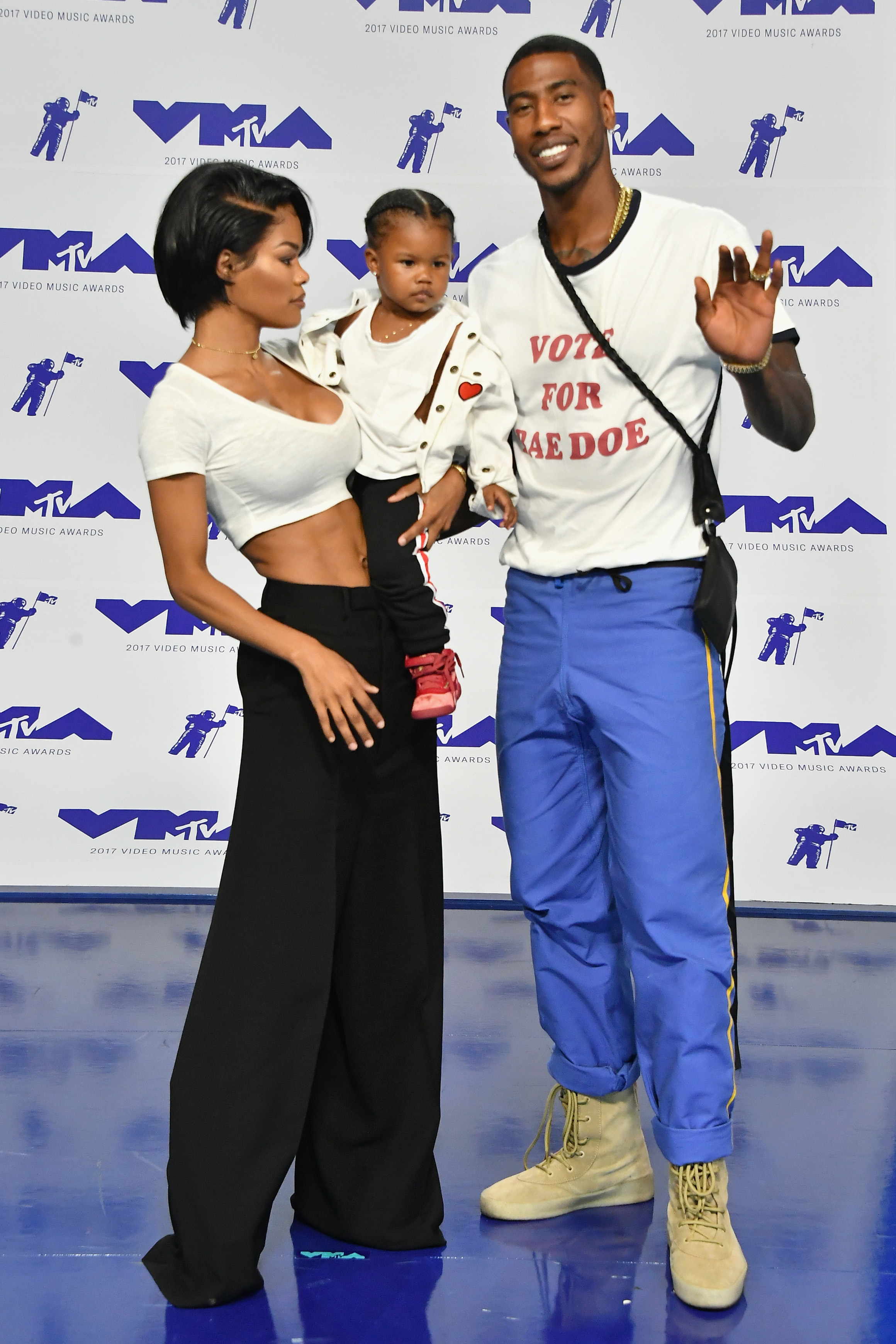 Teyana Taylor, Iman Shumpert, and Iman Tayla "Junie" Shumpert Jr. attend the MTV Video Music Awards in Inglewood. Teyana holds Junie as Iman smiles and waves on the blue carpet.