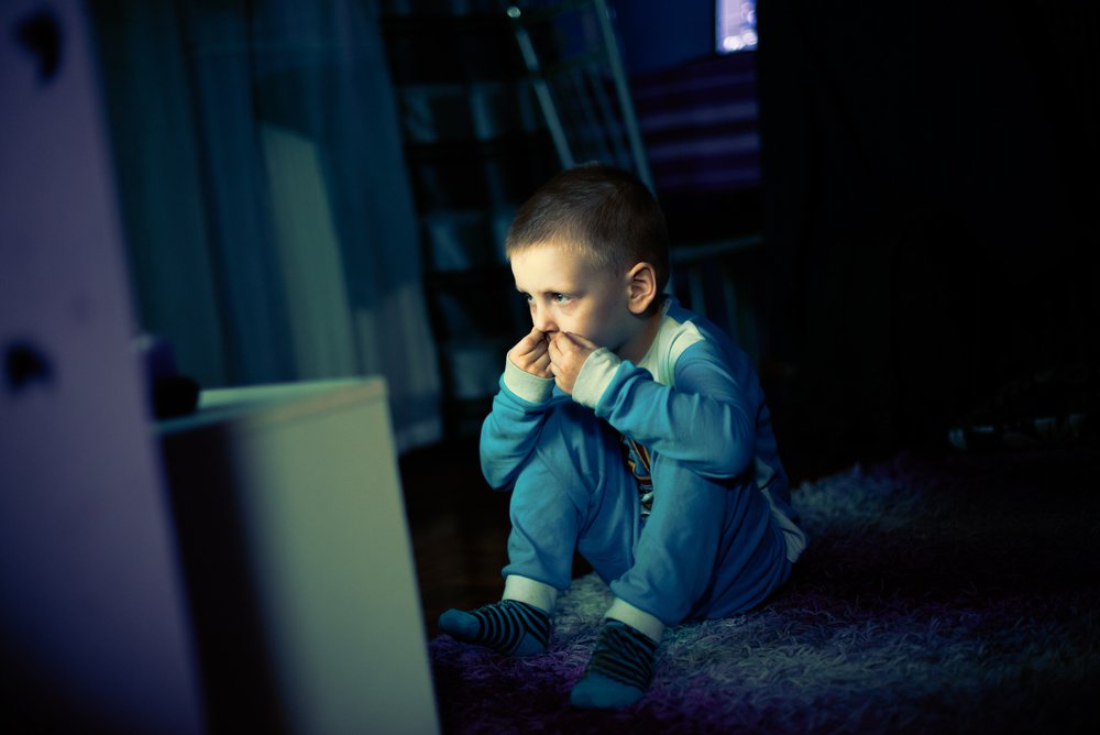 A sad little boy scared of the dark and watching the television. | Photo: Shteerstock.