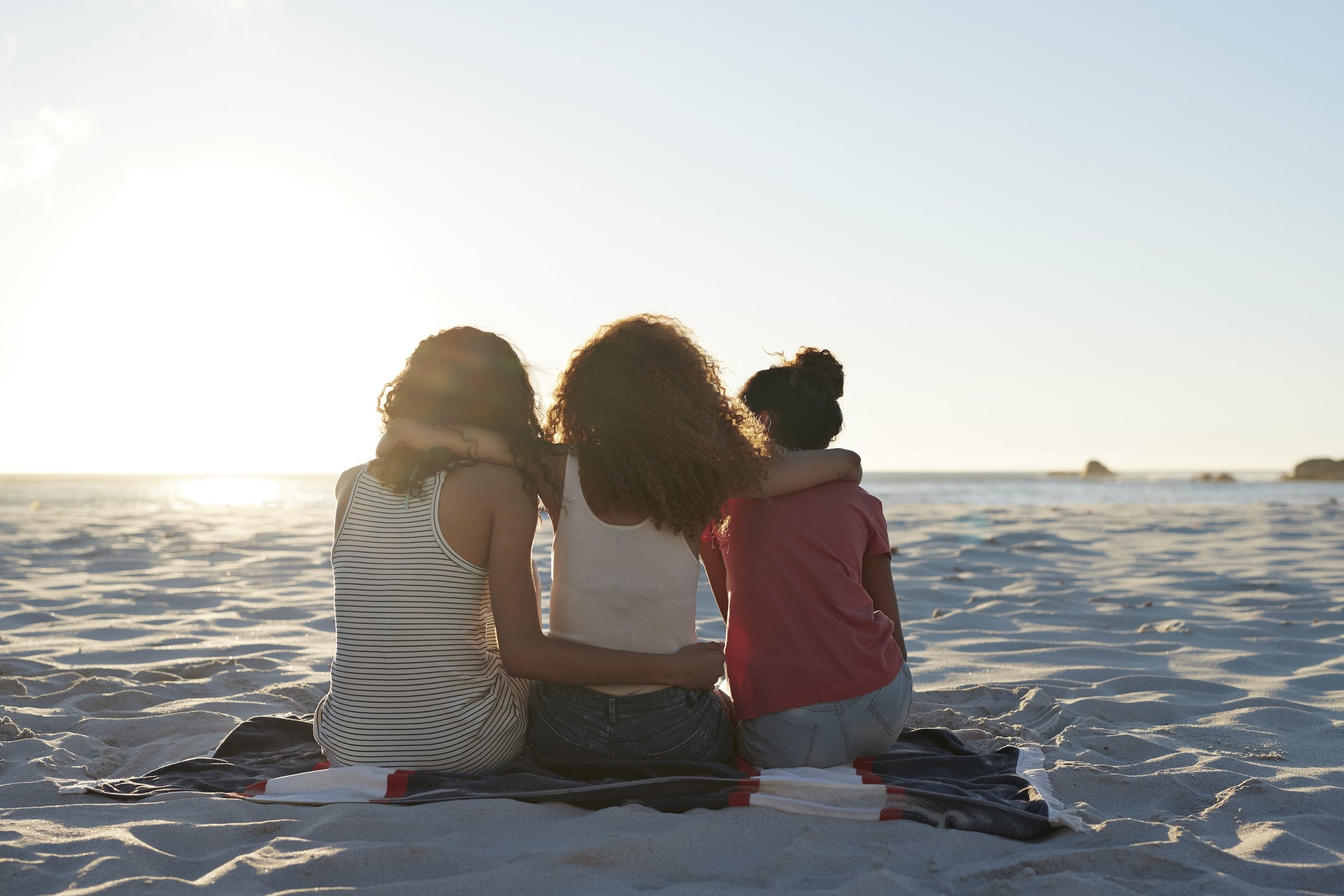 Rear view of three young women sitting on the beach. | Photo: Getty Images