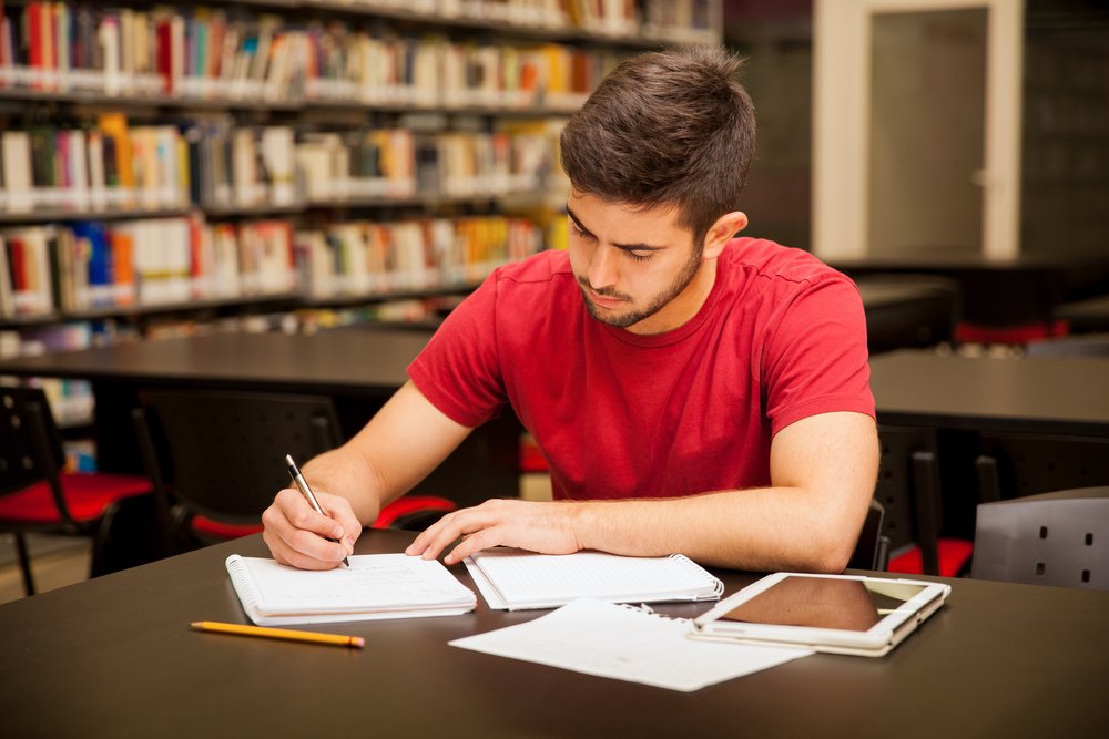 Joven estudiando en una biblioteca rodeado de libros. | Foto: Shutterstock