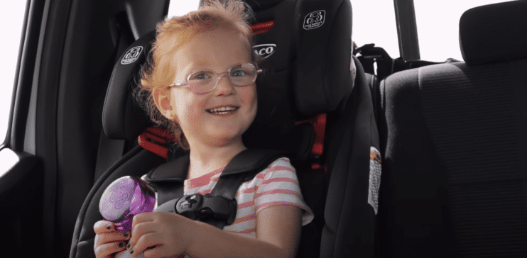 Hazel Busby pictured in her car seat, during a conversation with her dad, Adam Busby. 2019. | Photo: YouTube/its a Buzz World