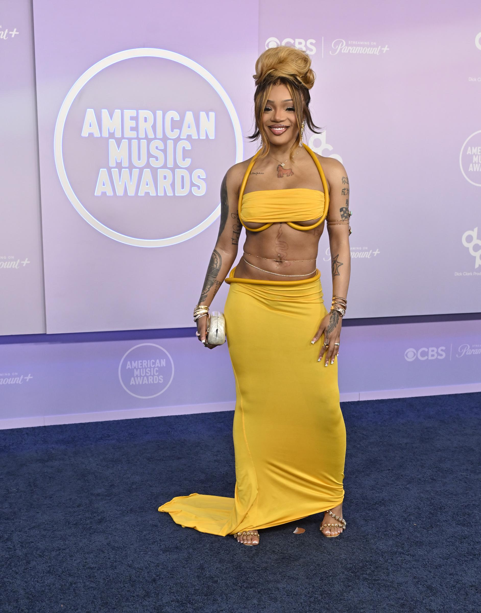 GloRilla turned heads in a vibrant yellow two-piece ensemble with bold cutouts and draped fabric that highlighted her tattooed silhouette. Her towering beehive hairstyle and stacked jewelry added even more drama to the daring look.